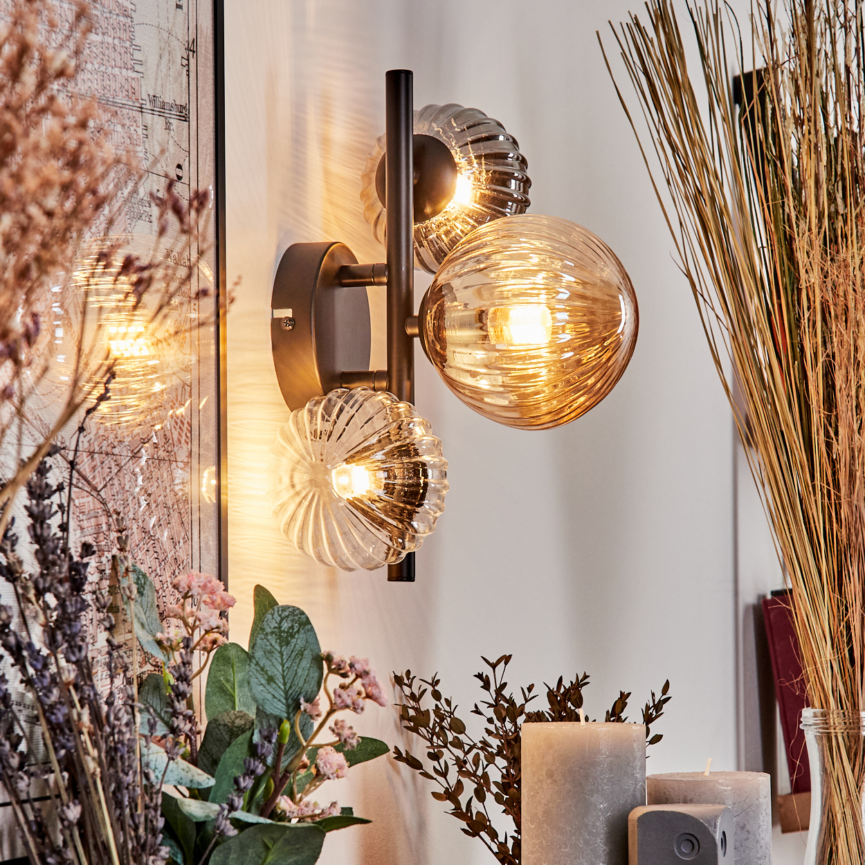 Wandlampe mit drei bernsteinfarbenen Glaskugeln. Blumen und Karte im Hintergrund.