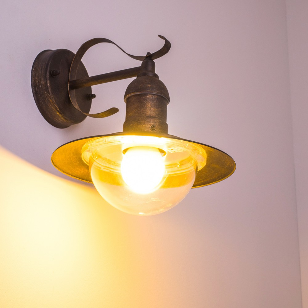 Verzierte bronzefarbene Wandlampe mit heller Glühbirne an einer weißen Wand. Lampe hat einen weißen Globus.
