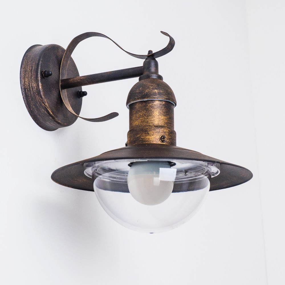 Bronzefarbene Außenwandleuchte mit klarem, halbkugelförmigem Schirm. An weißer Wand montiert.