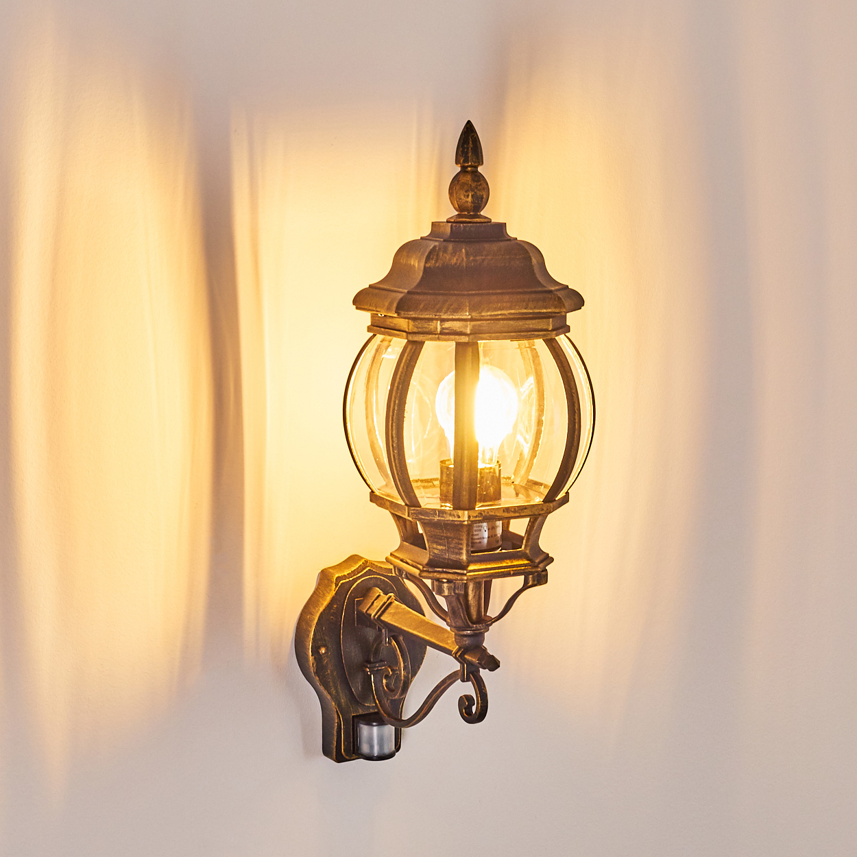 Außenwandleuchte, beleuchtet und wirft Schatten auf eine weiße Wand.