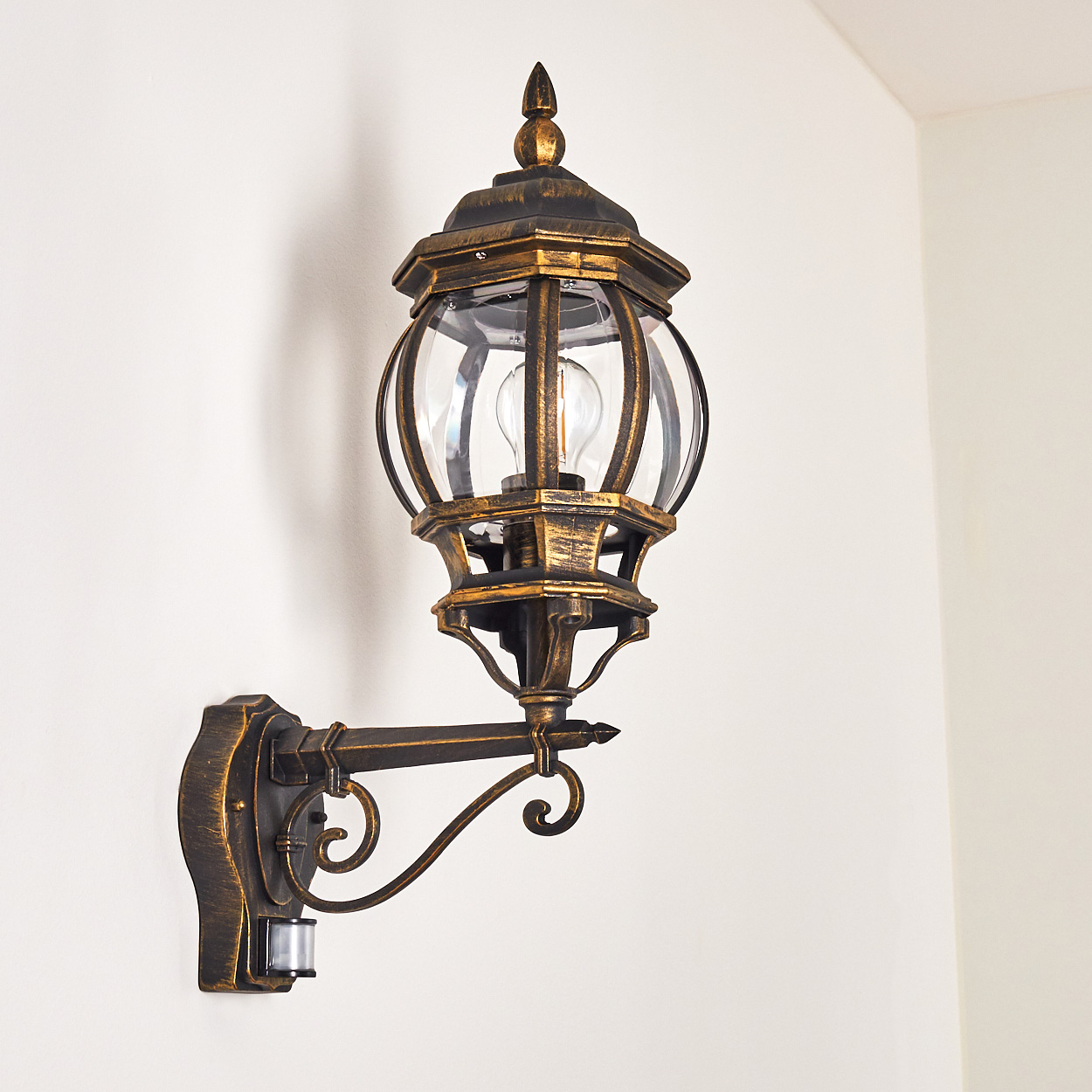 Bronze-Wandleuchte mit Glaspaneelen. Sie ist an einer weißen Wand montiert.