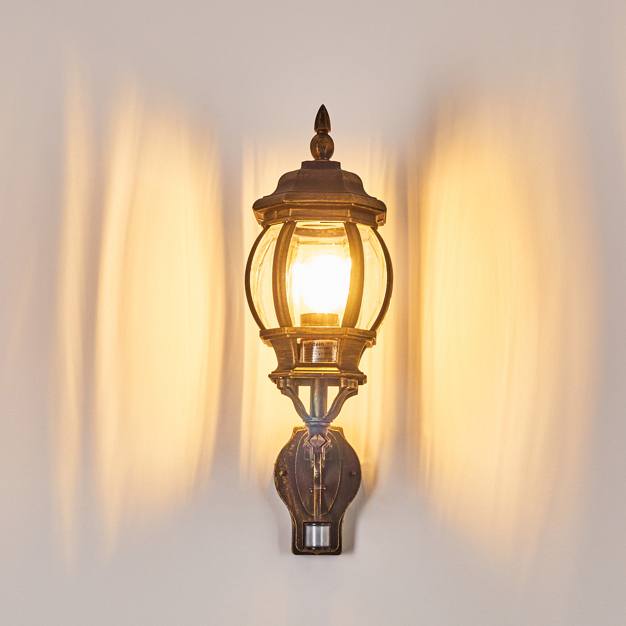Außenwandleuchte, beleuchtet und wirft Schatten auf eine weiße Wand.