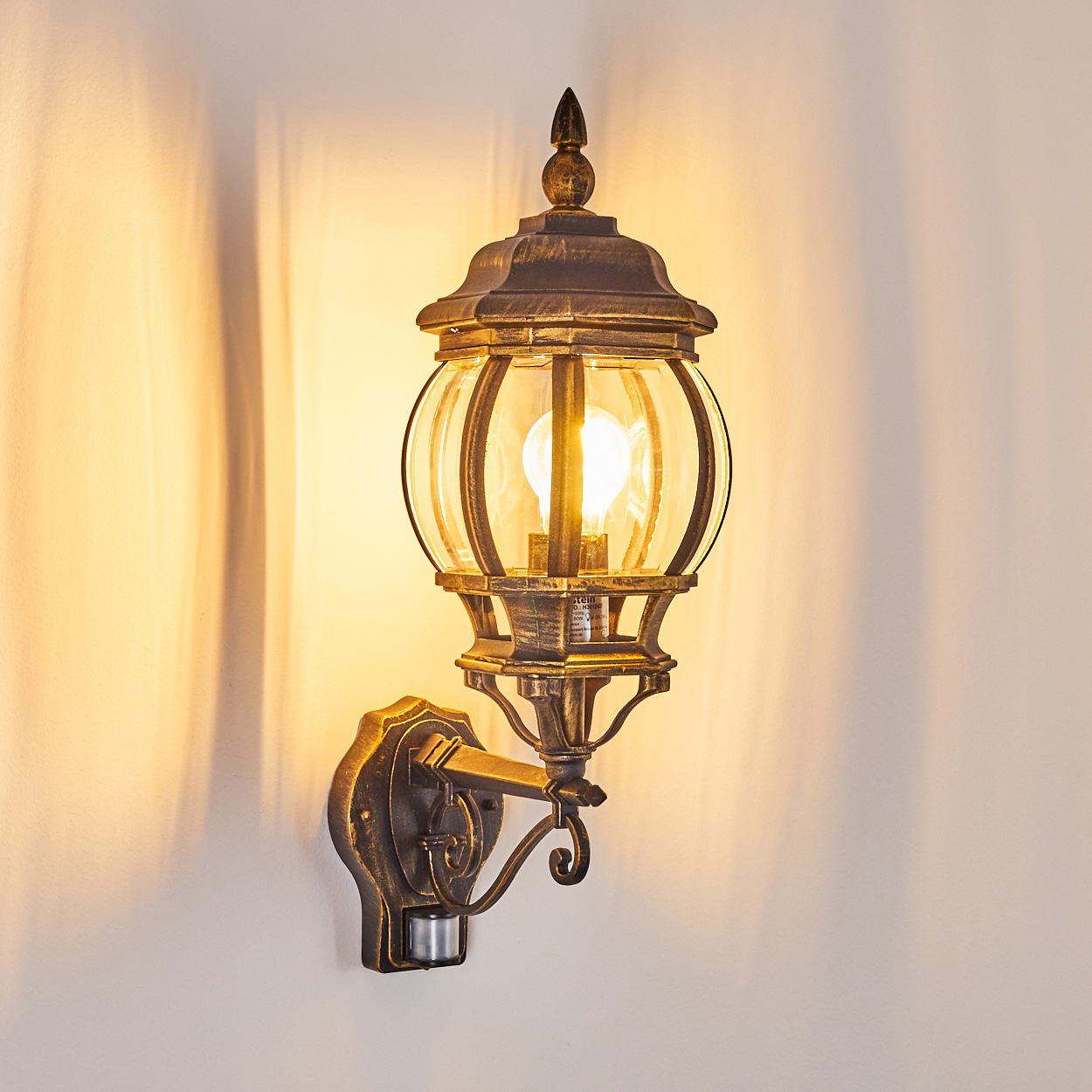 Außenwandleuchte, beleuchtet und wirft Schatten auf eine weiße Wand.