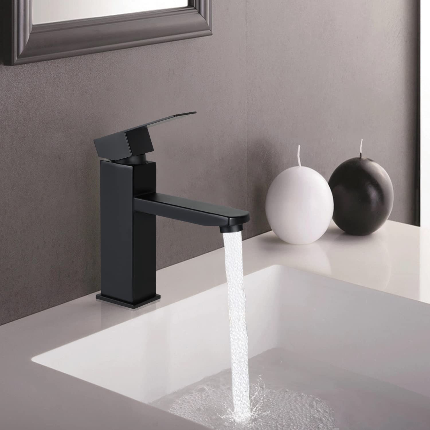 Ein schwarzer Wasserhahn mit Wasser, das in ein weißes Waschbecken fließt. Zwei Kerzen im Hintergrund.