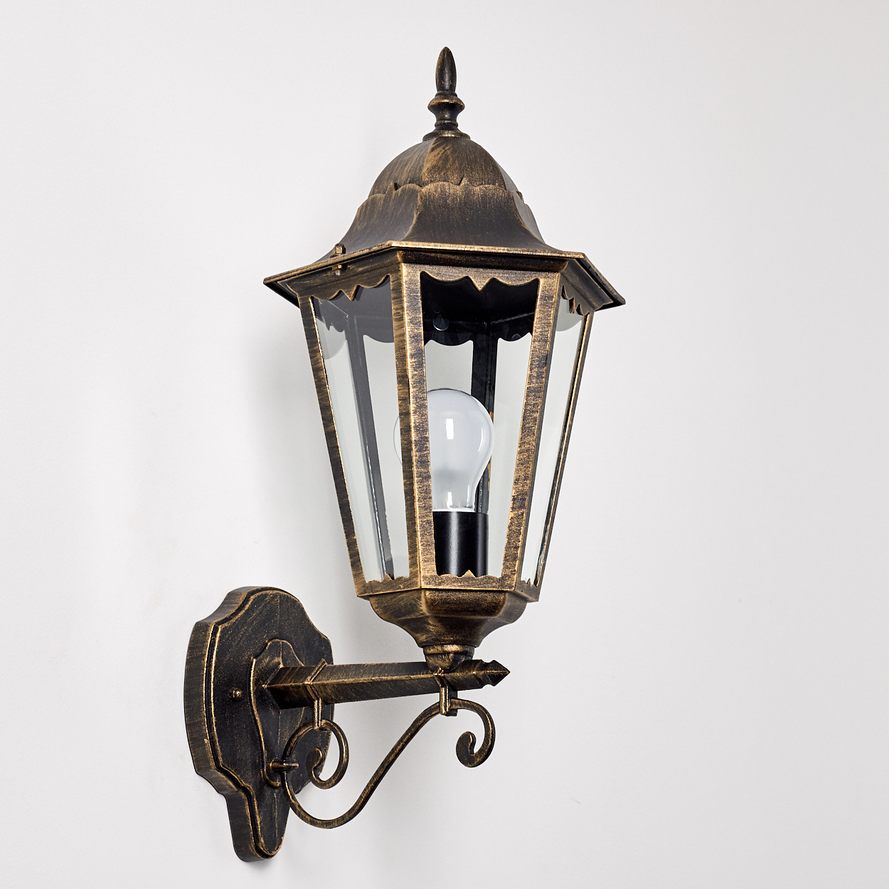 Wandlampe mit goldenem Rahmen, Glasscheiben und Glühbirne. An einer weißen Wand.
