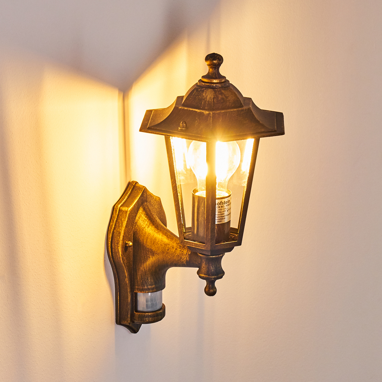 Bronze-Außenlampe an weißer Wand. Glühbirne innen. Es hat einen Bewegungssensor.