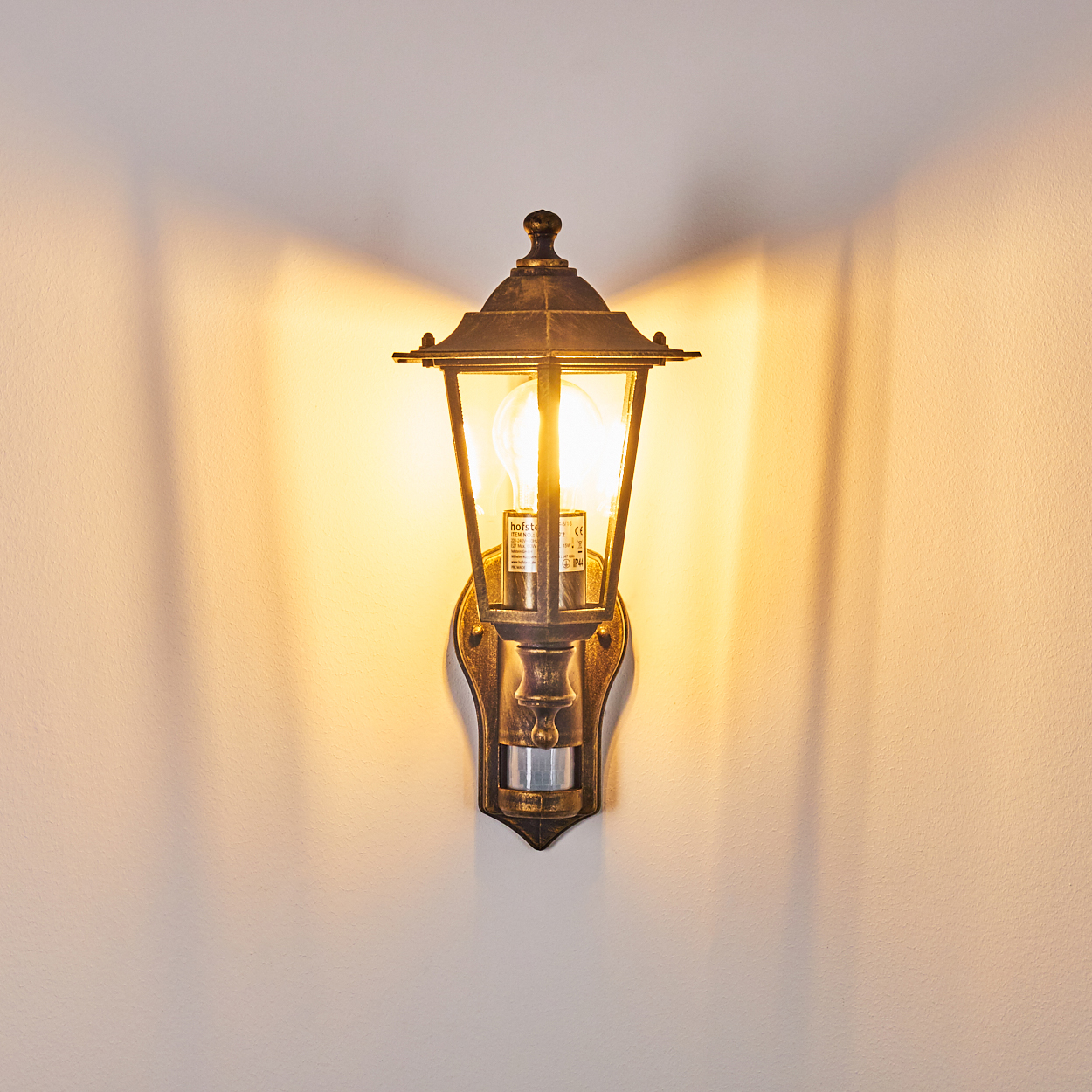 Beleuchtete Bronze-Außenwandleuchte, wirft Schatten an die Wand.