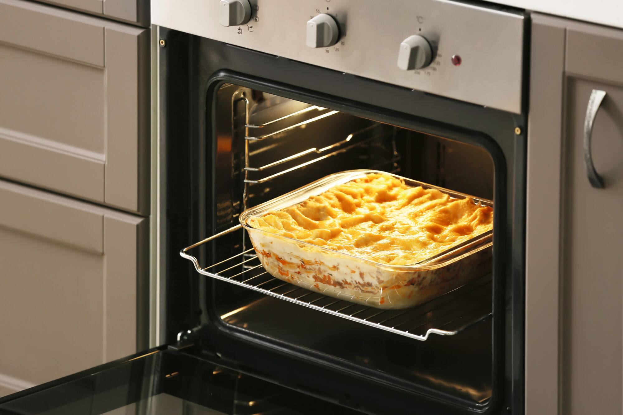 Ofen mit offener Tür, Glasgericht mit Lasagne auf dem Rost.