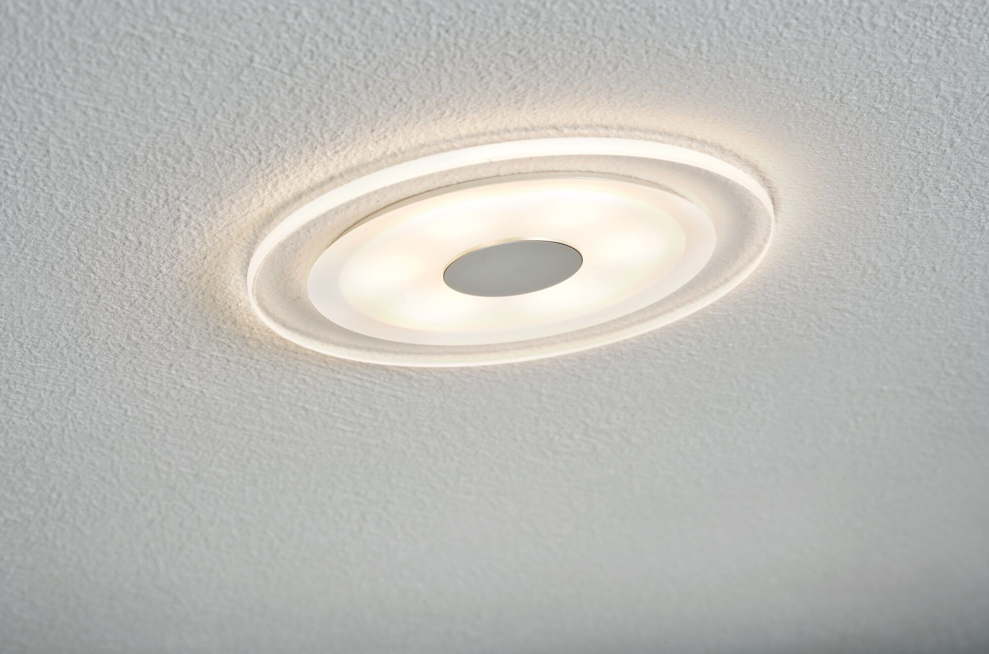 Eine weiße, kreisförmige Deckenlampe mit zentralem Licht und einem Ring darum, an einer strukturierten Decke.