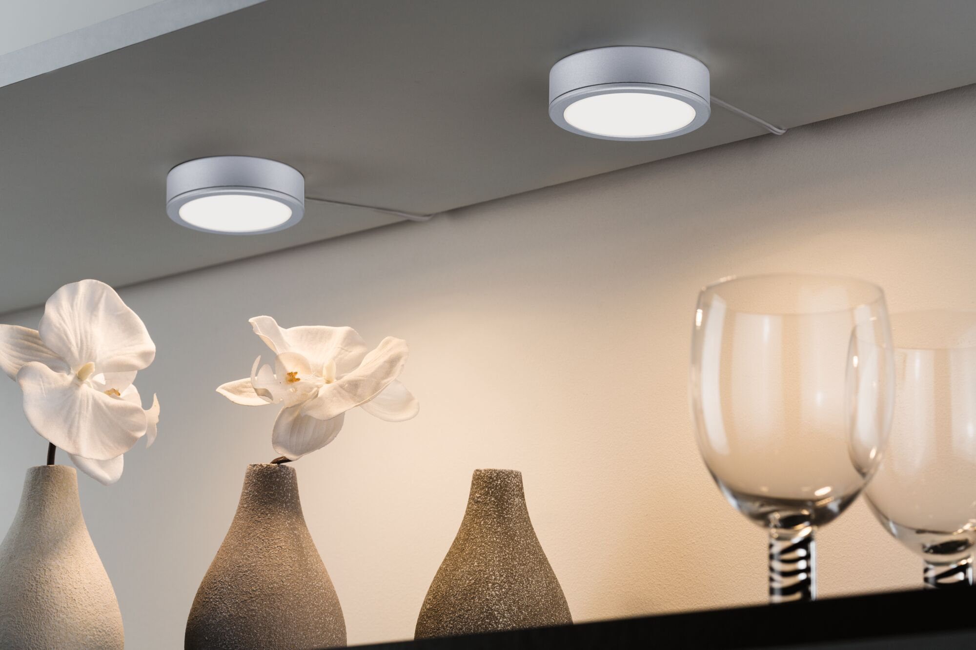 Zwei kreisförmige Lichter auf einer grauen Oberfläche, mit Vasen und Gläsern im Vordergrund.
