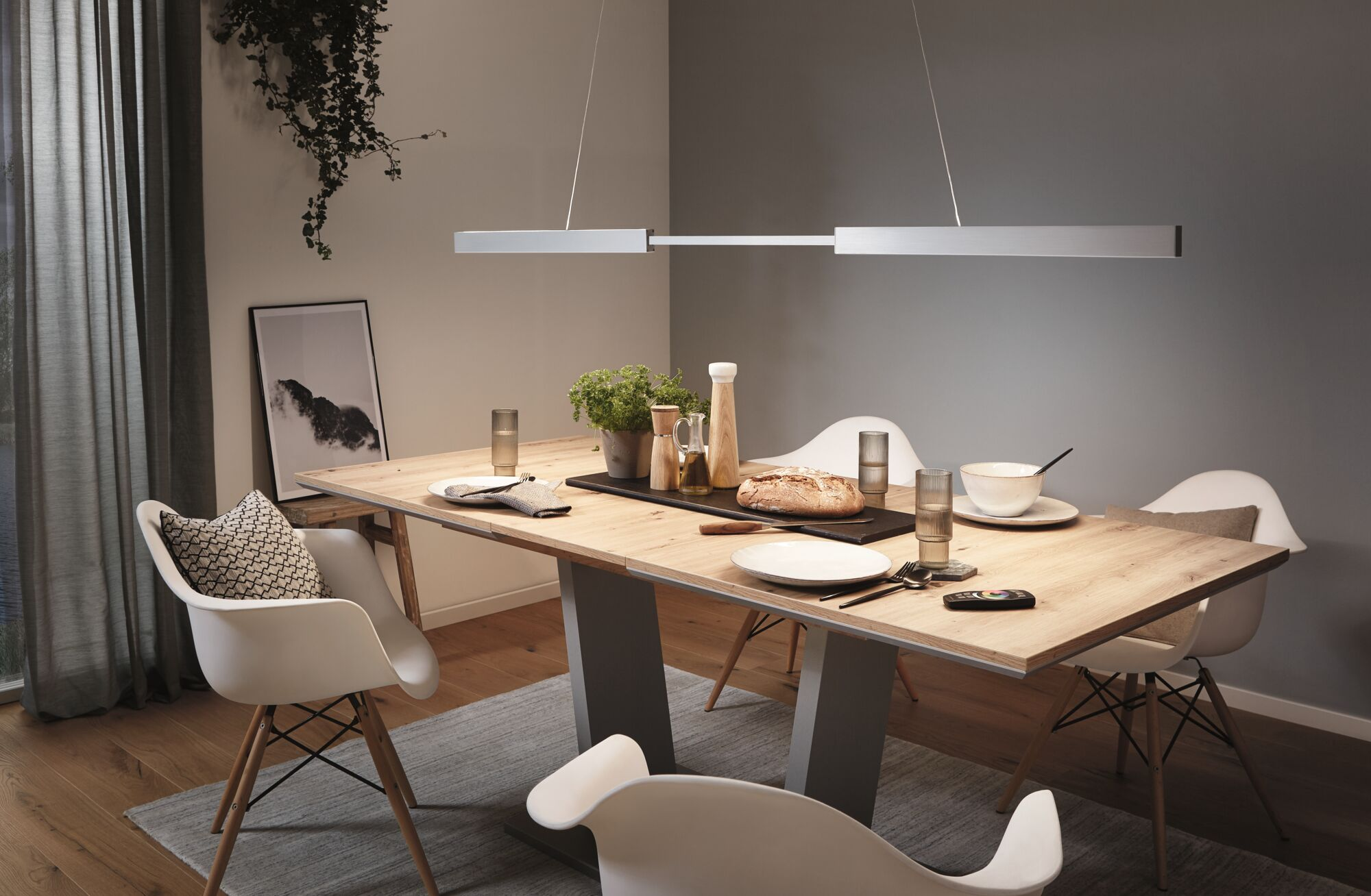 Une table à manger avec une lampe suspendue au-dessus. Il y a des assiettes et des verres.