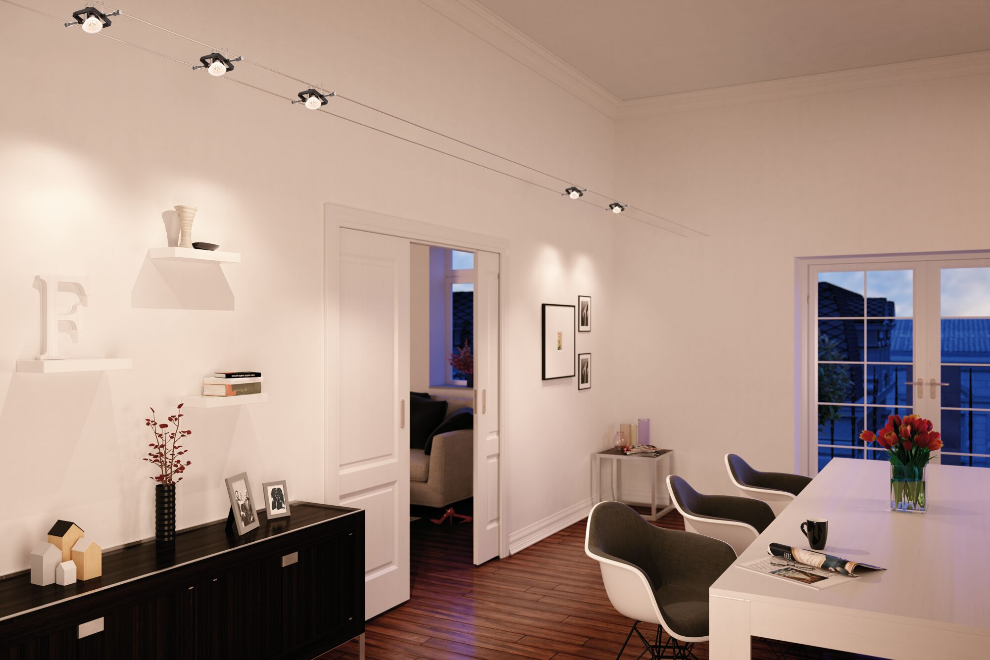 Jasny pokój z oświetleniem szynowym na suficie, półkami i stołem. Drzwi prowadzą do innego pokoju.