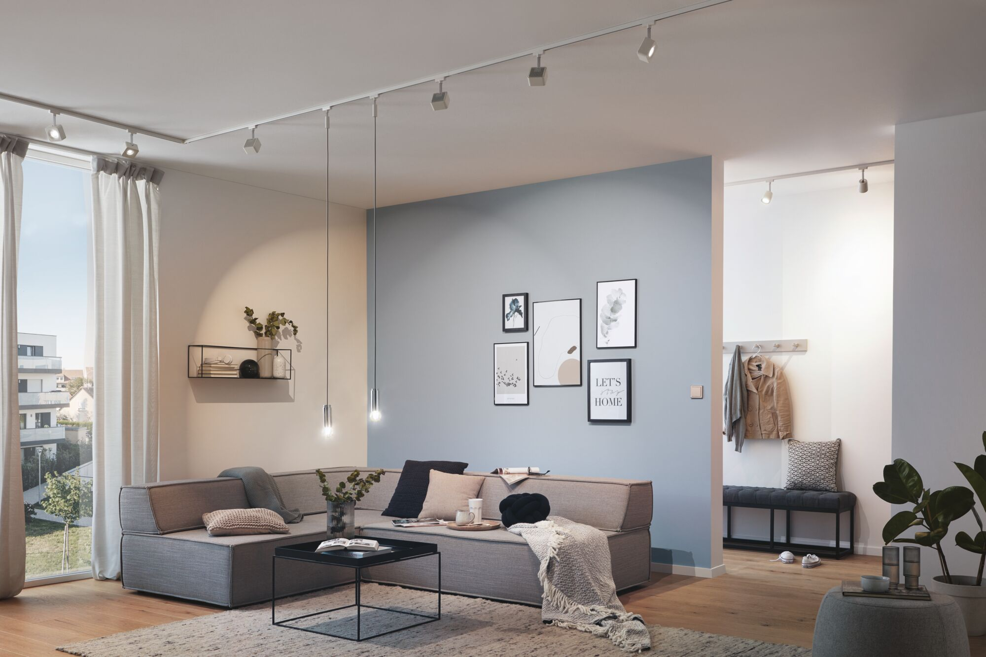 Wohnzimmer mit grauem Sofa, Kunstwerken und einem Schienensystem an der Decke.