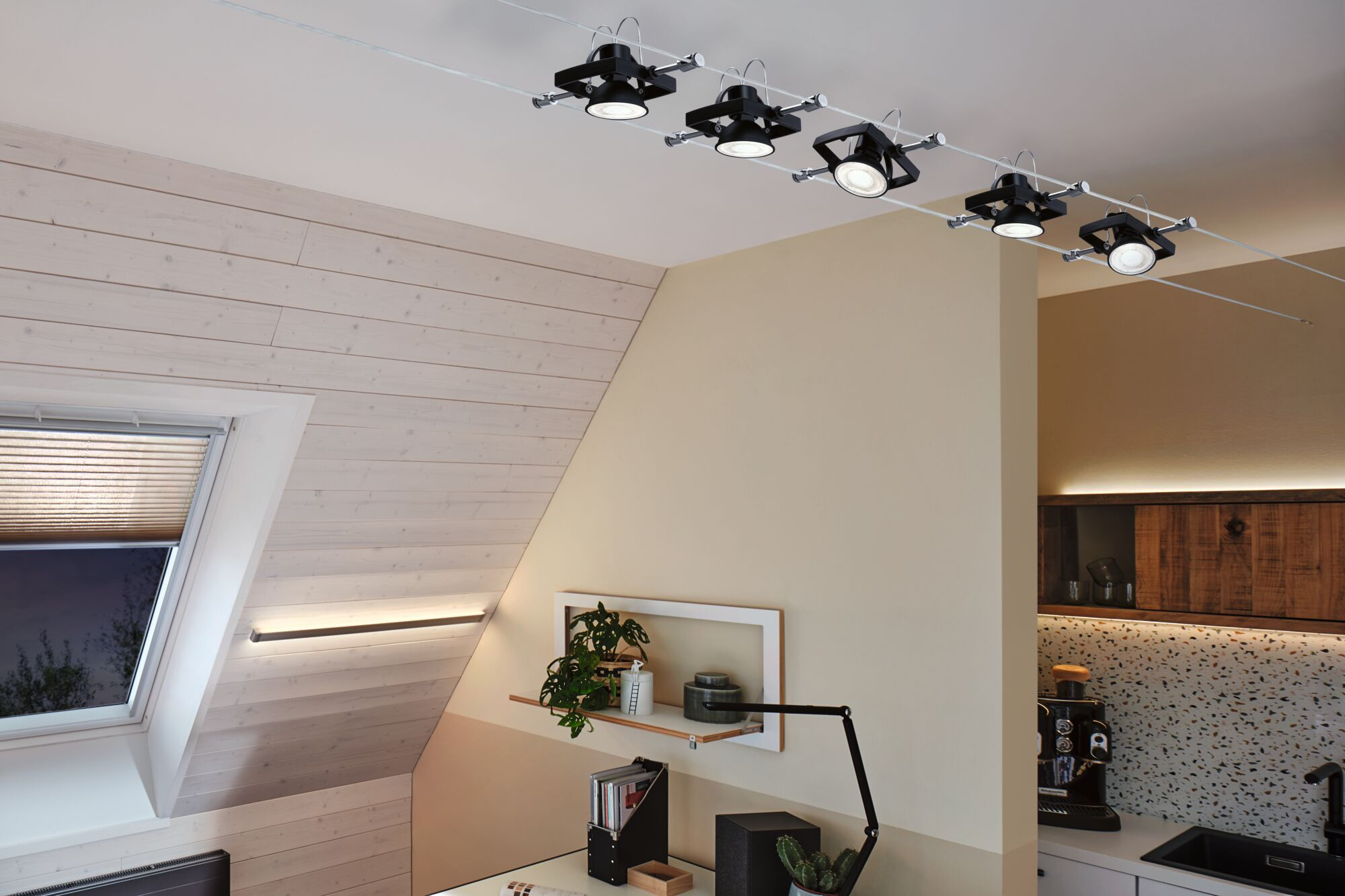 Ein Dachzimmer mit Schienenbeleuchtung und einem Schreibtisch mit Lampe und Pflanze.