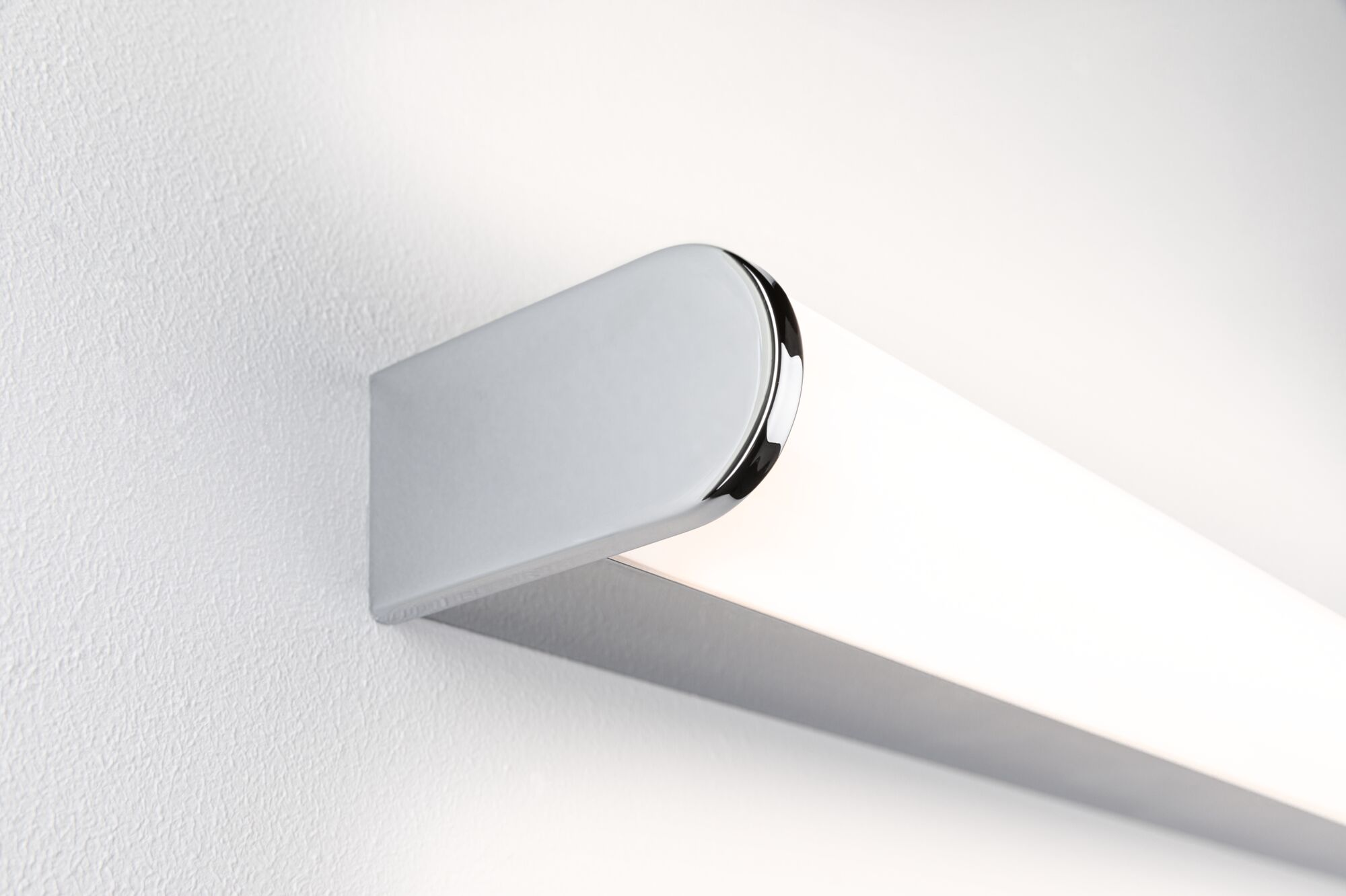 Eine weiße und chromfarbene LED-Leuchte an einer weißen Wand, Seitenansicht.