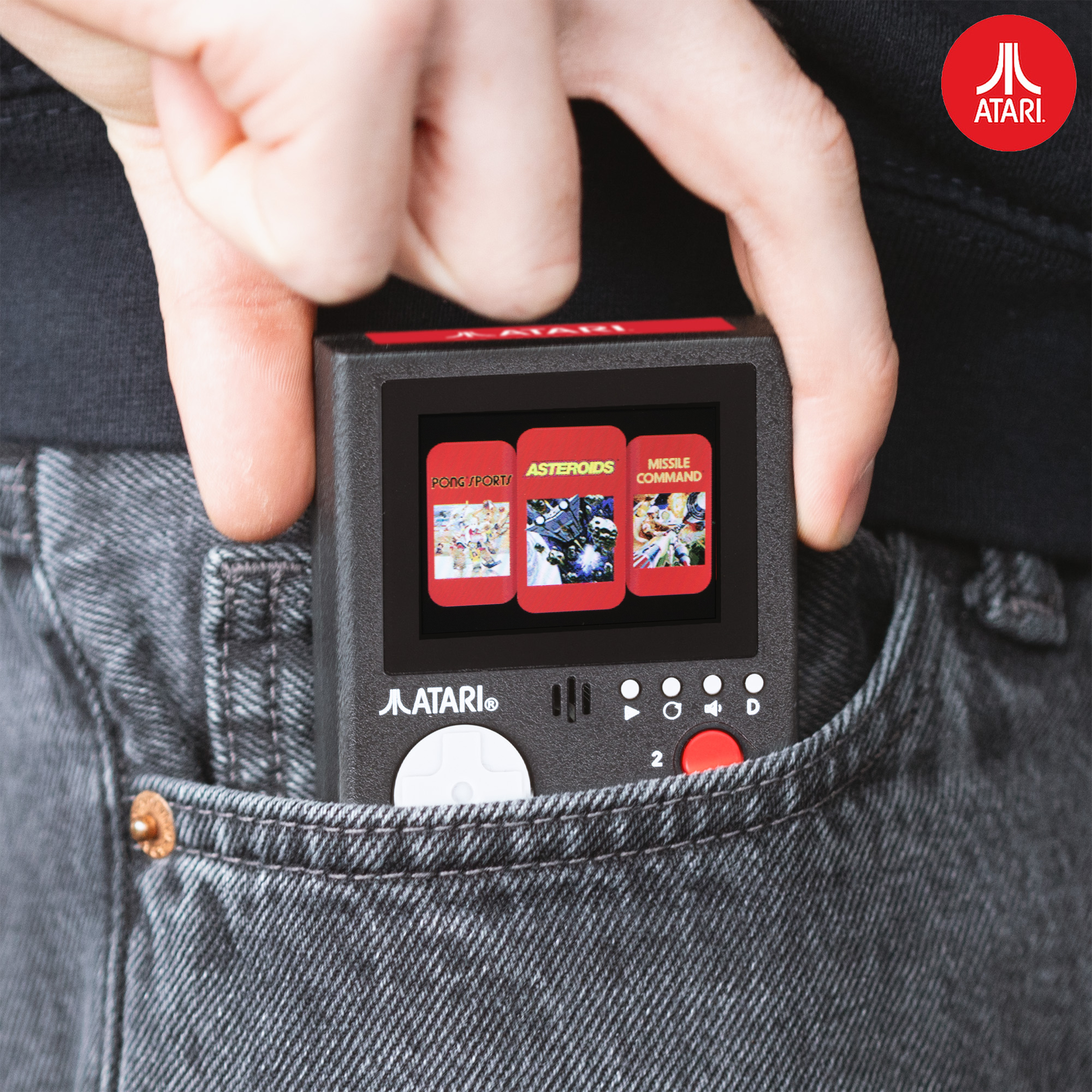 A person's hand holding a small black game console. The game has three games: Pong, Asteroids, and Missile Command.