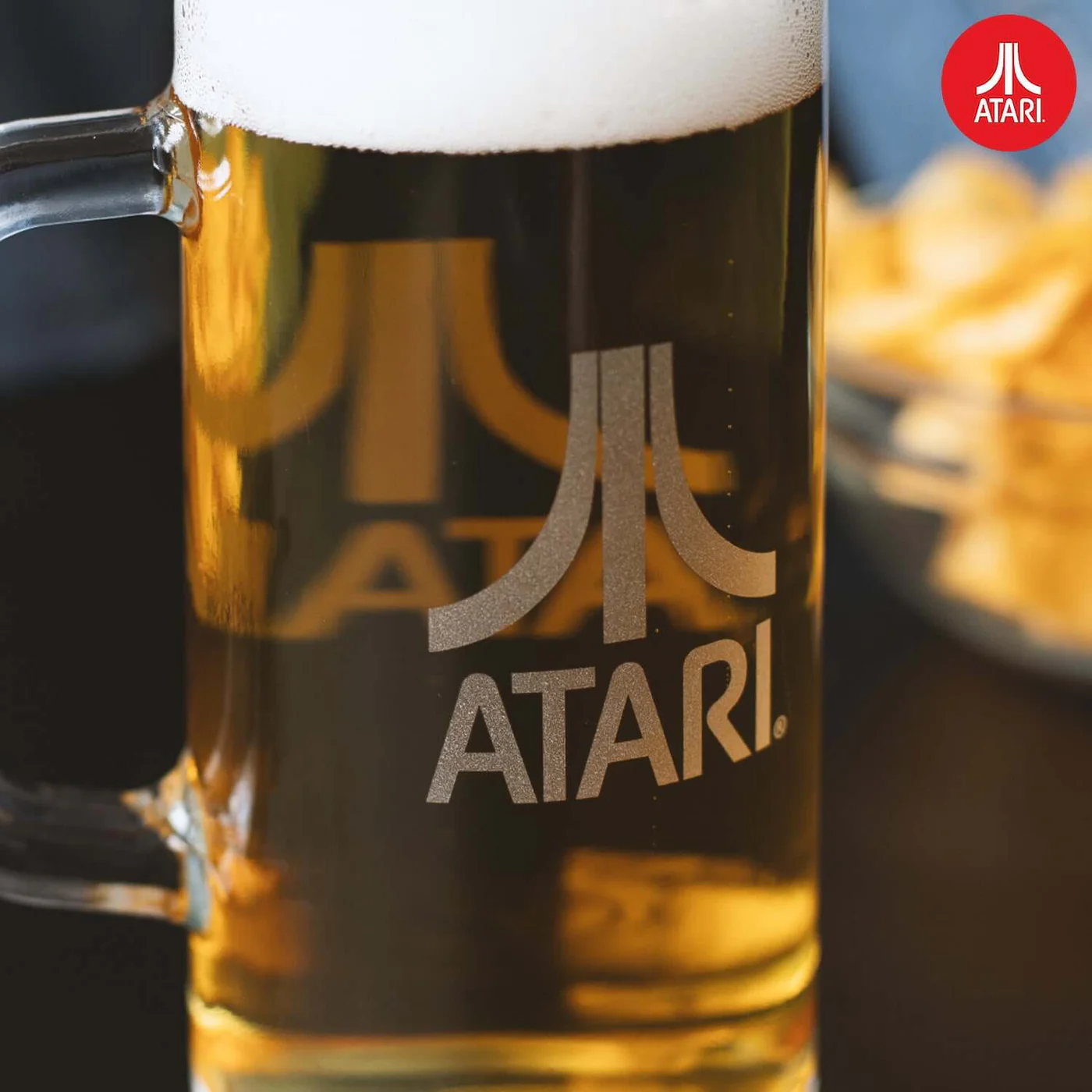 Close-up van een Atari bierglas gevuld met bier. Atari logo op het glas. Chips op de achtergrond.