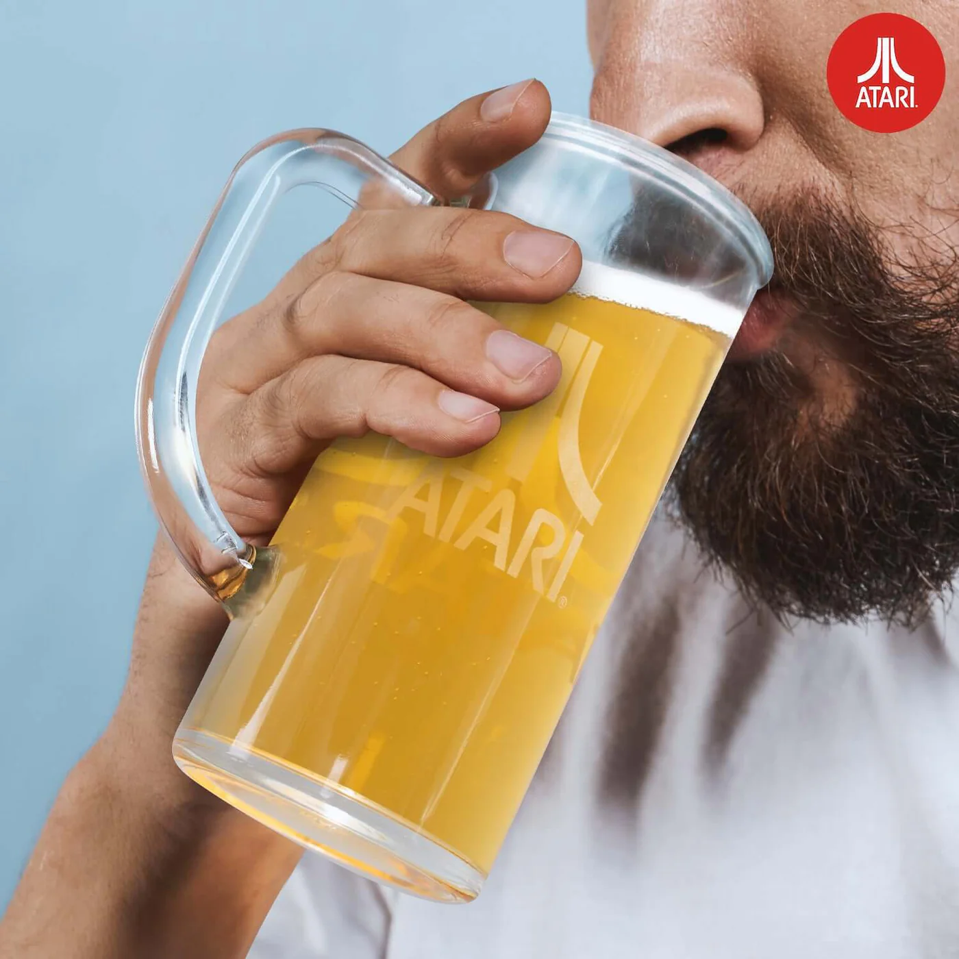 Een man die bier drinkt uit een Atari bierglas. Atari logo op het glas, blauwe achtergrond.
