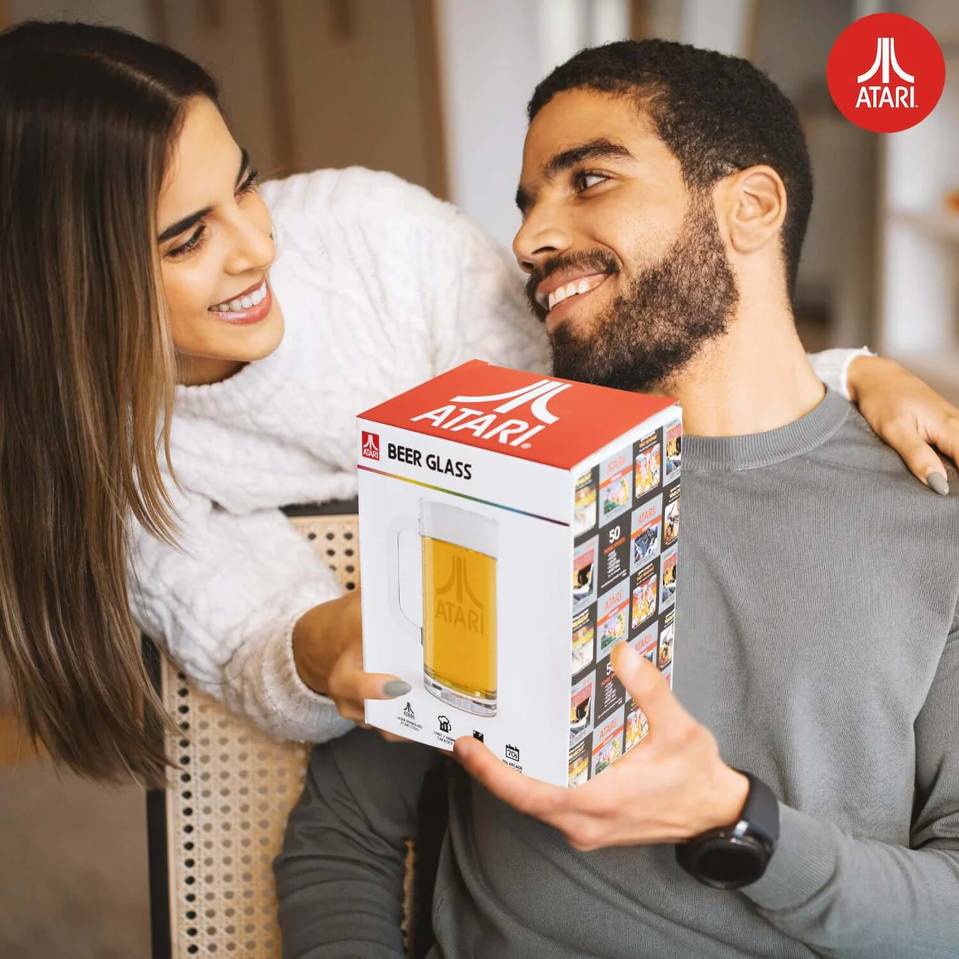 Een man en een vrouw die een Atari bierglasdoos vasthouden. De doos heeft Atari logo's en een bierglas erop.