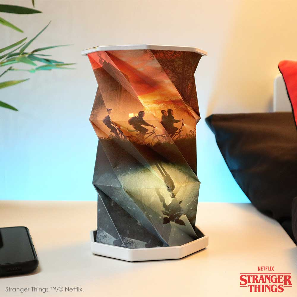 Gedraaide lamp met Stranger Things-afbeelding, met mensen op fietsen. Geplaatst op een wit oppervlak met een zwarte telefoon.