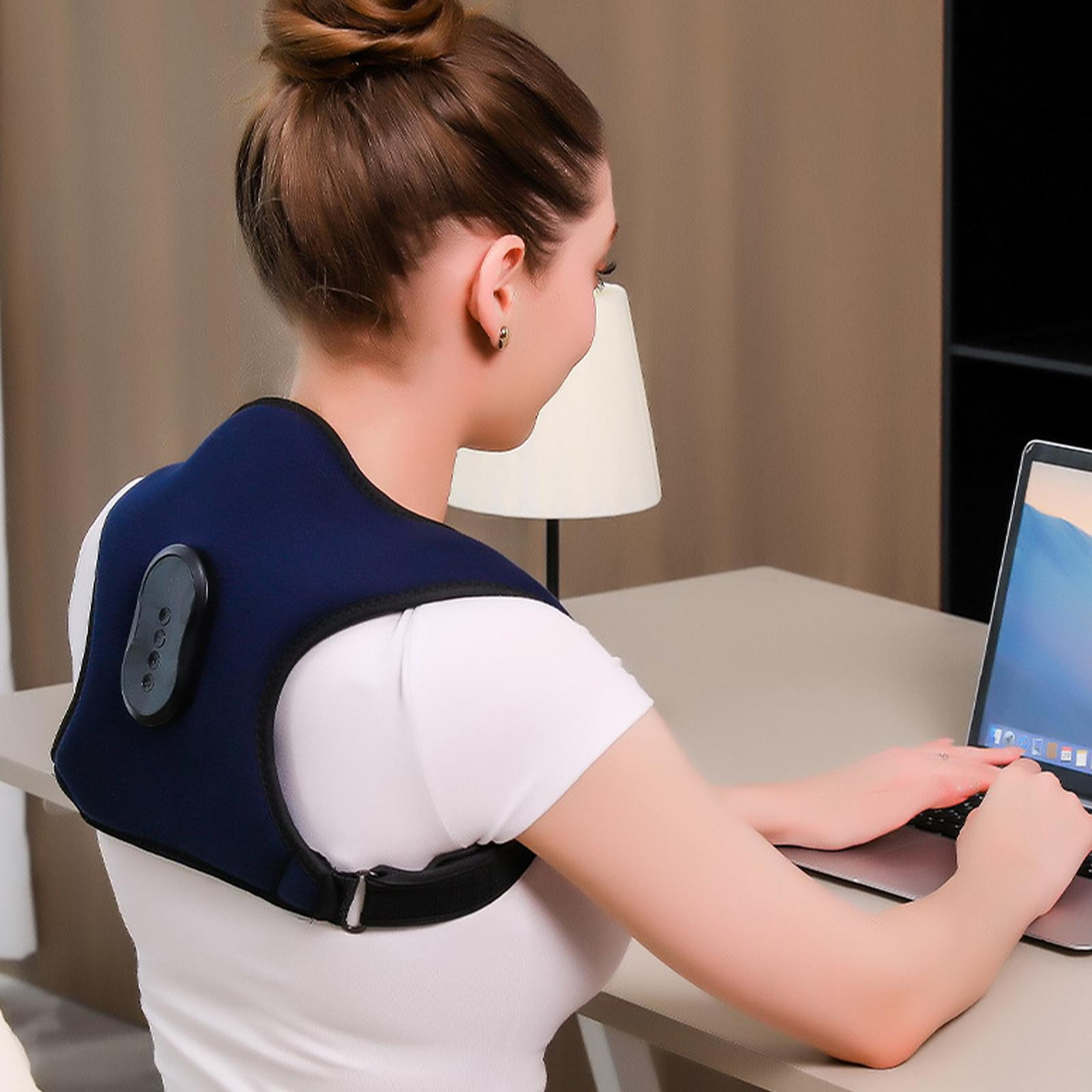 Frau trägt ein blaues Nackenmassagegerät und benutzt einen Laptop am Schreibtisch in einem Raum.
