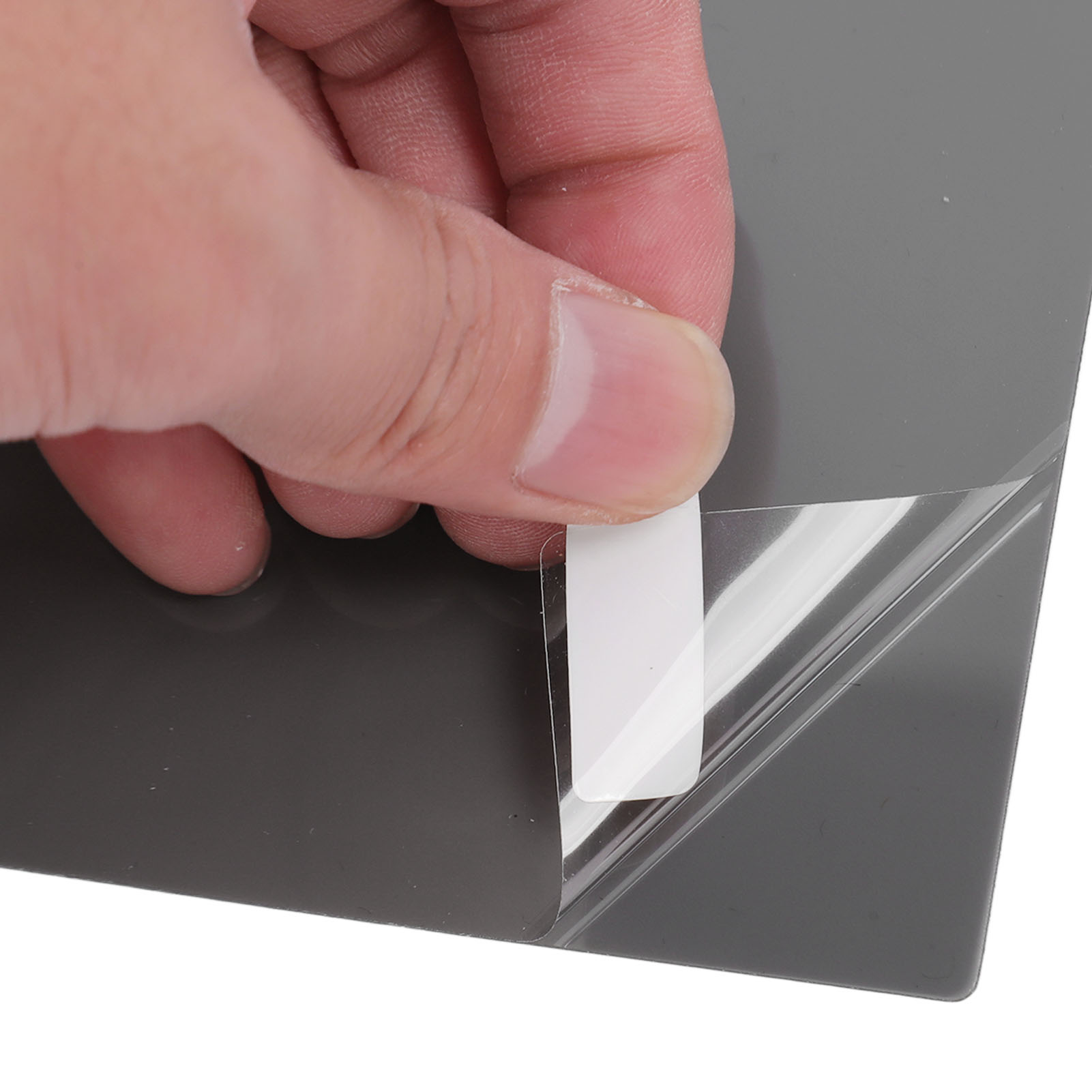 Eine Hand, die eine Schutzfolie von einem grauen, rechteckigen Klebefolie abzieht.