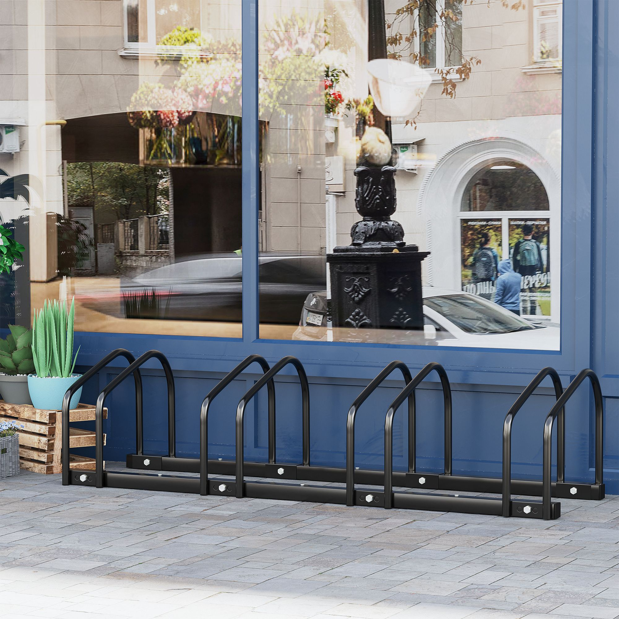 Schwarzer Fahrradständer auf einem Bürgersteig, blauer Gebäudehintergrund mit Reflexionen, Grün und Blumen.