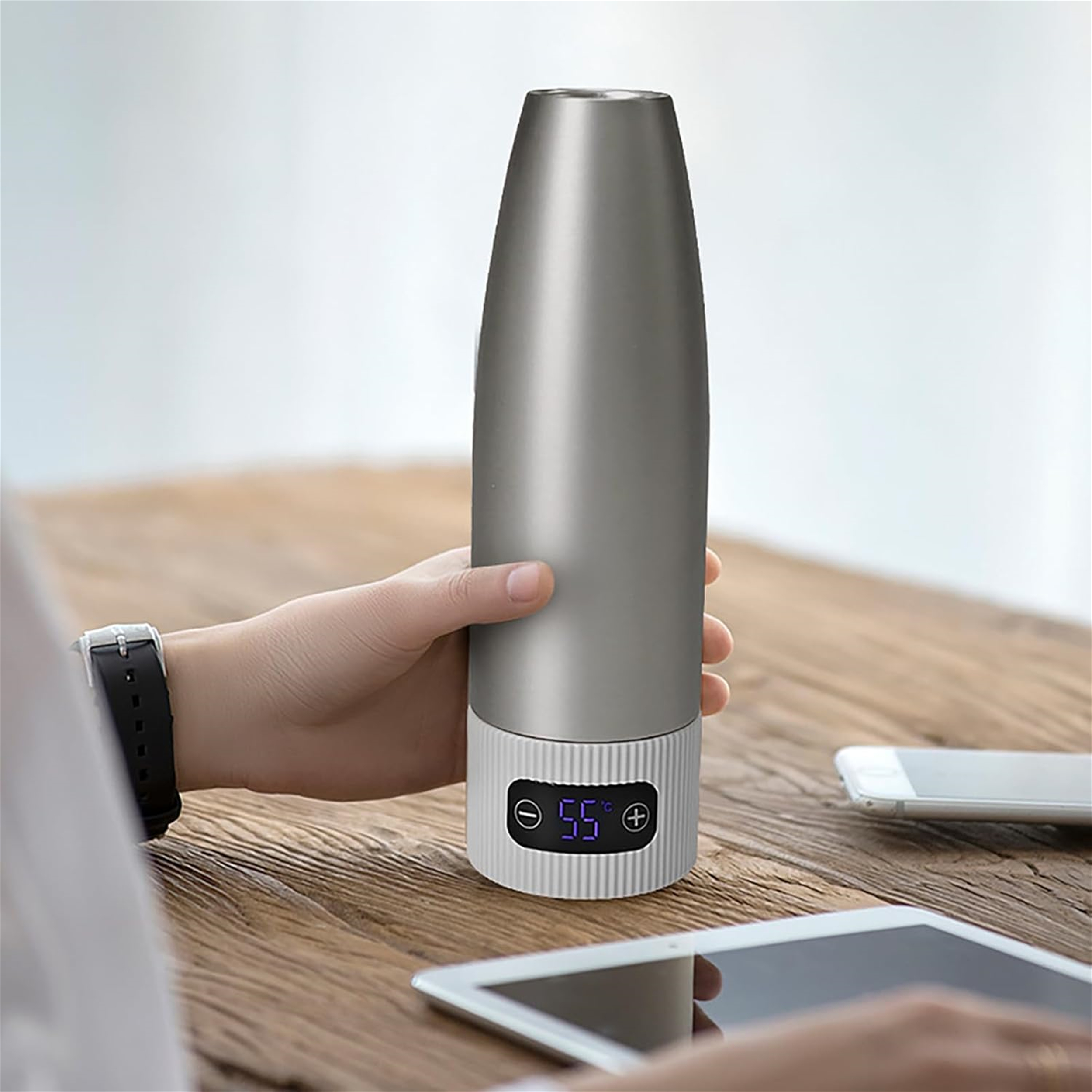 Eine Person hält eine graue isolierte Wasserflasche mit Digitalanzeige auf einem Holztisch.