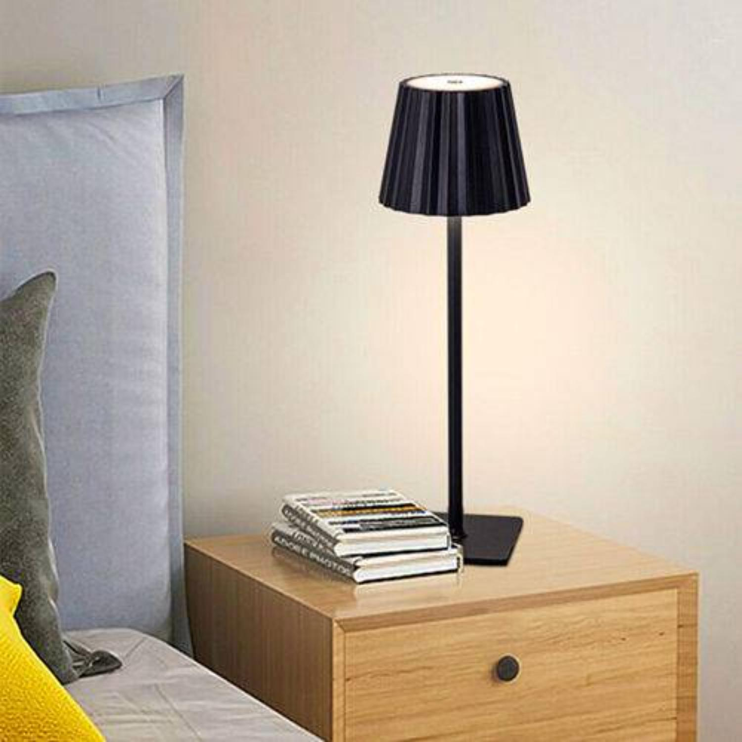 Schwarze Lampe auf einem Nachttisch mit Büchern, im Hintergrund eine weiße Wand.