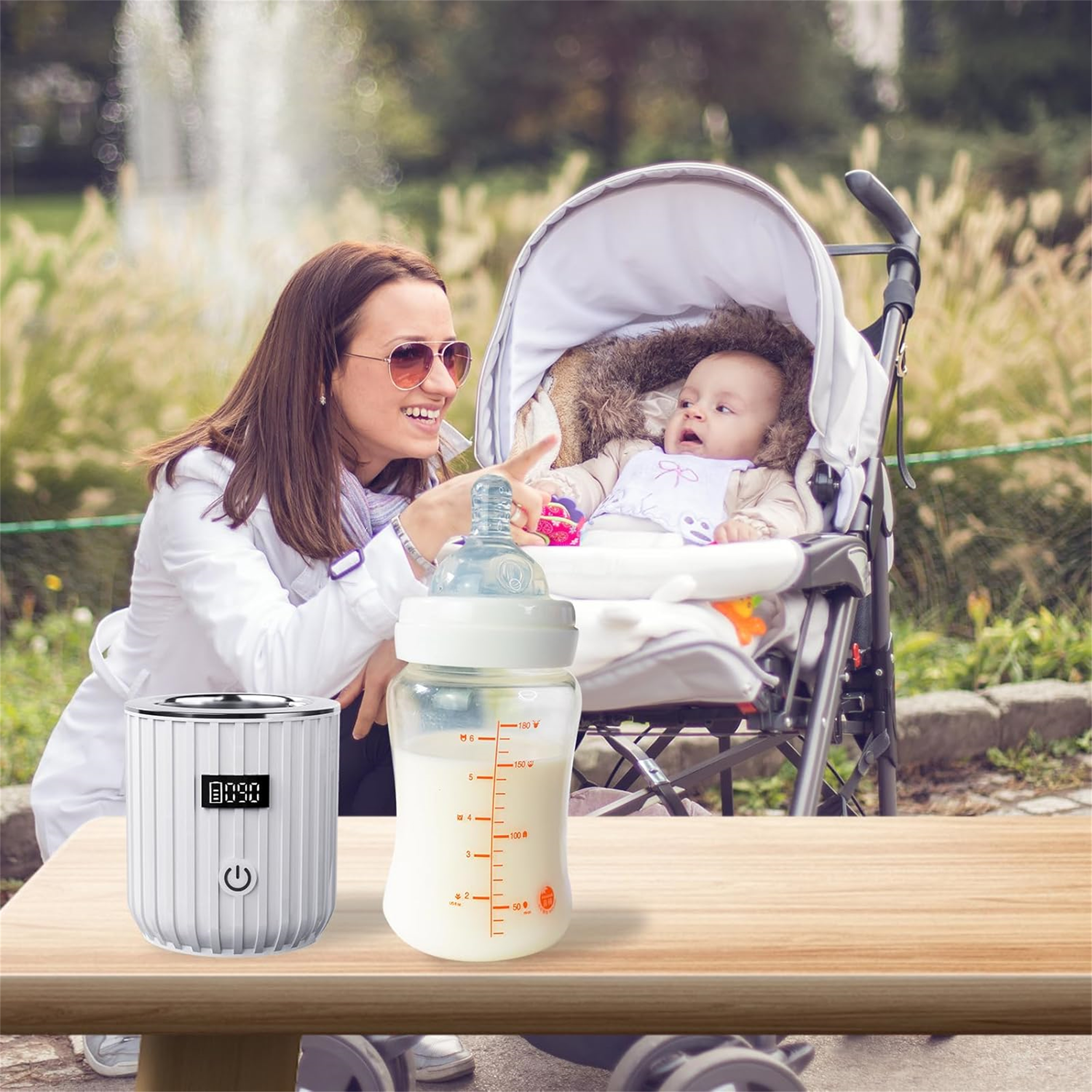 Frau mit Baby im Kinderwagen, Flaschenwärmer und Flasche mit Milch auf dem Tisch.