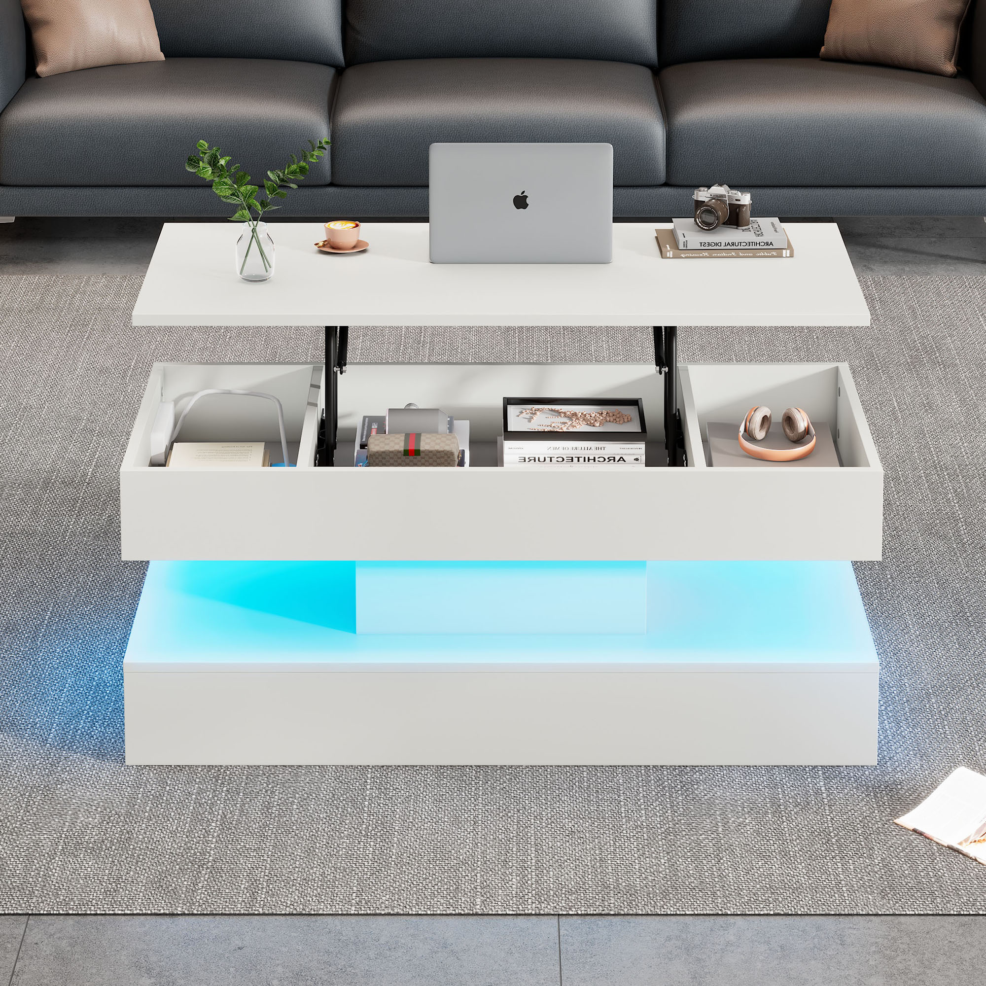 Weißer Couchtisch mit blauer LED-Beleuchtung. Die Oberseite öffnet sich und zeigt Stauraum. Laptop und Deko oben.