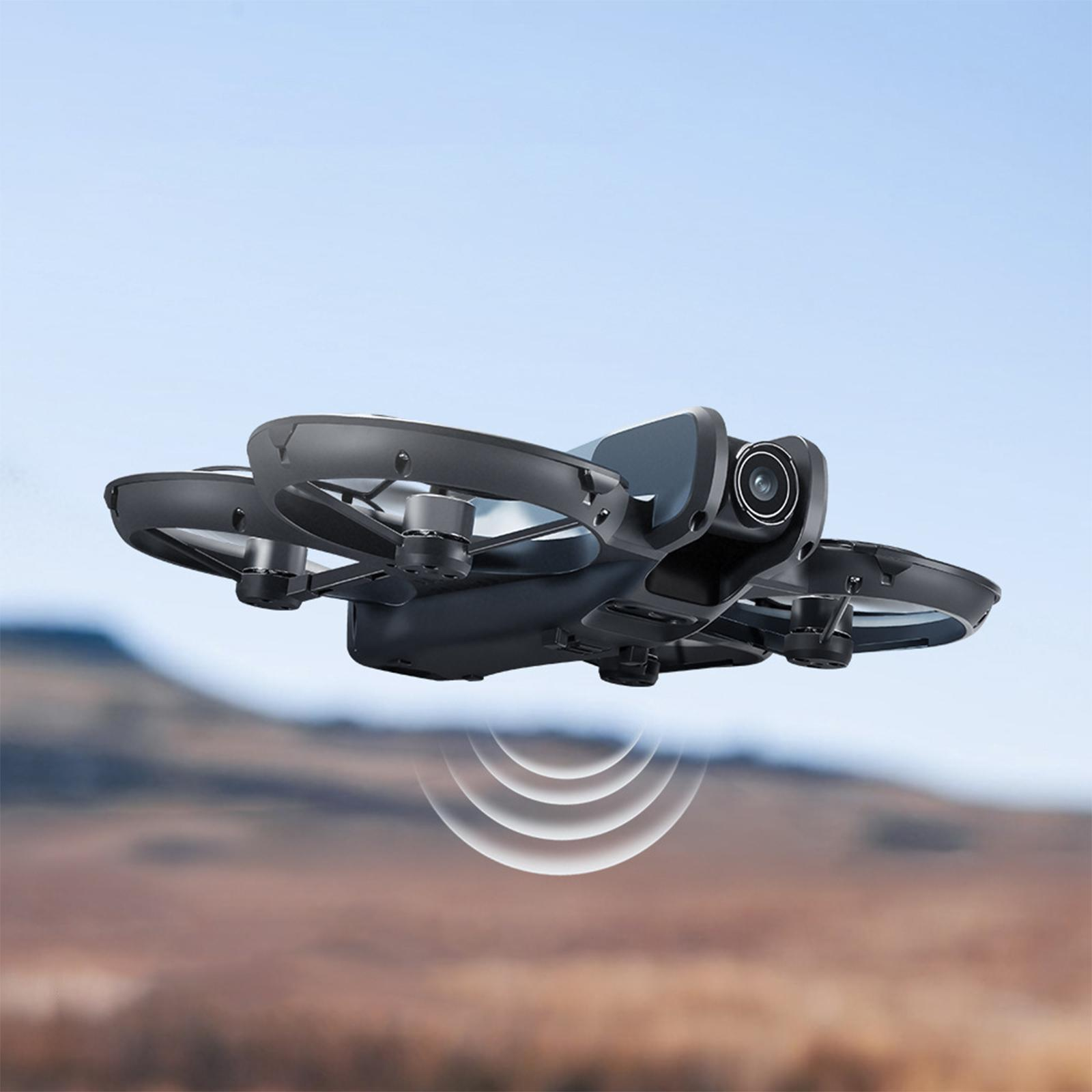 Eine schwarze Drohne im Flug vor verschwommenem Hintergrund mit Hügeln und blauem Himmel.