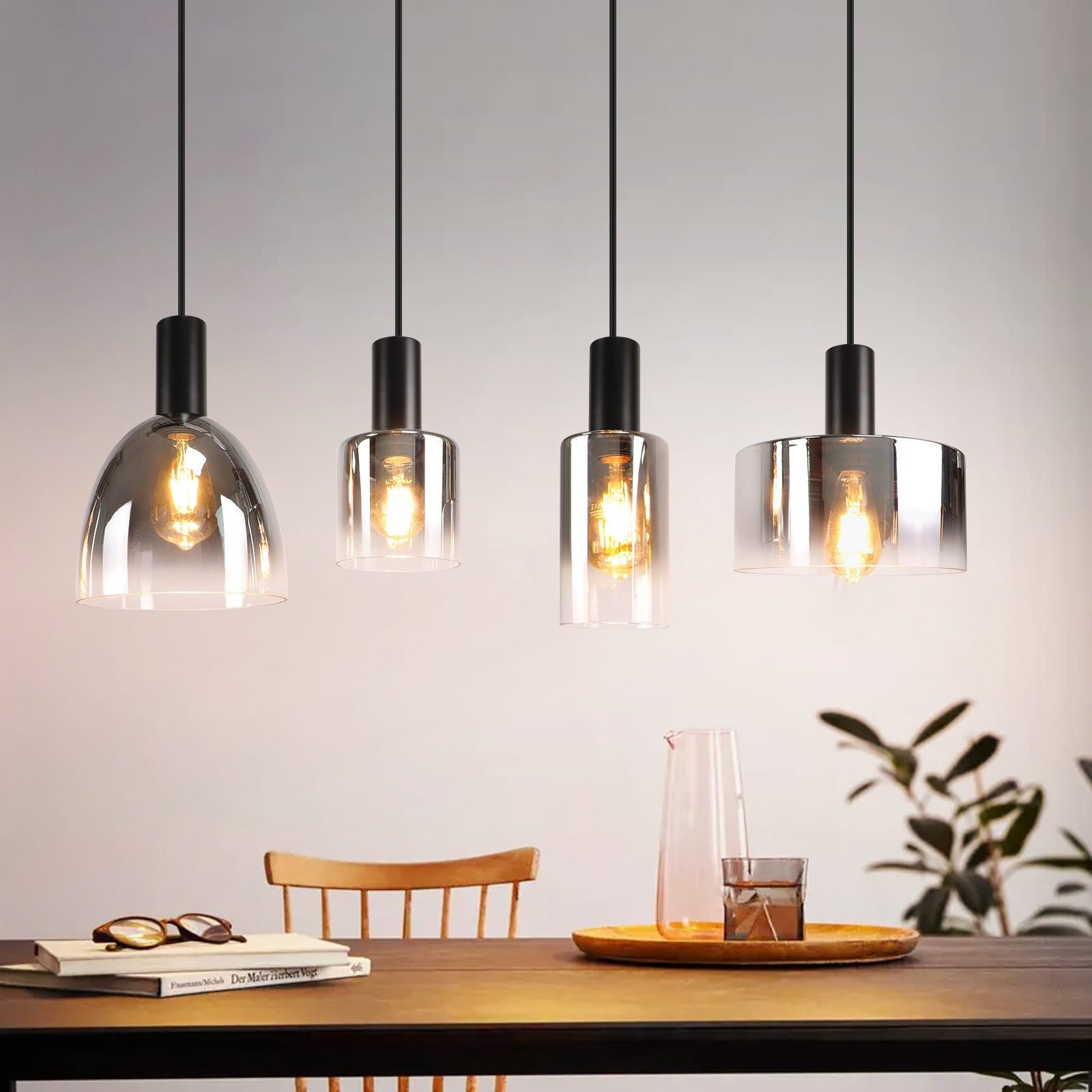 Quattro lampade a sospensione con paralumi in vetro trasparente. Luci accese.