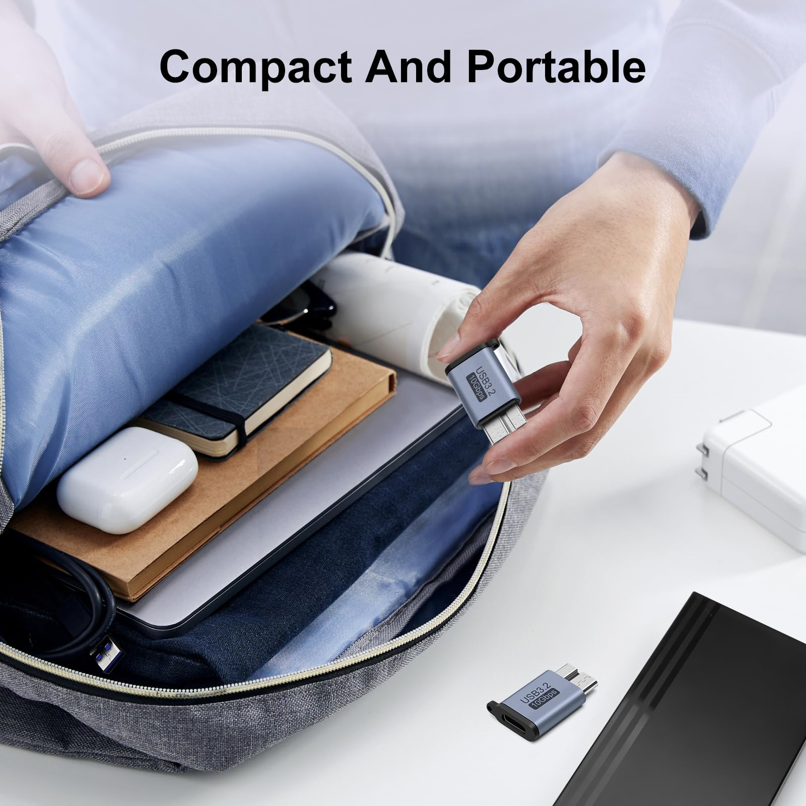 Eine Person hält einen USB-C-Adapter neben einem Rucksack. Andere Gegenstände sind in der Tasche sichtbar.