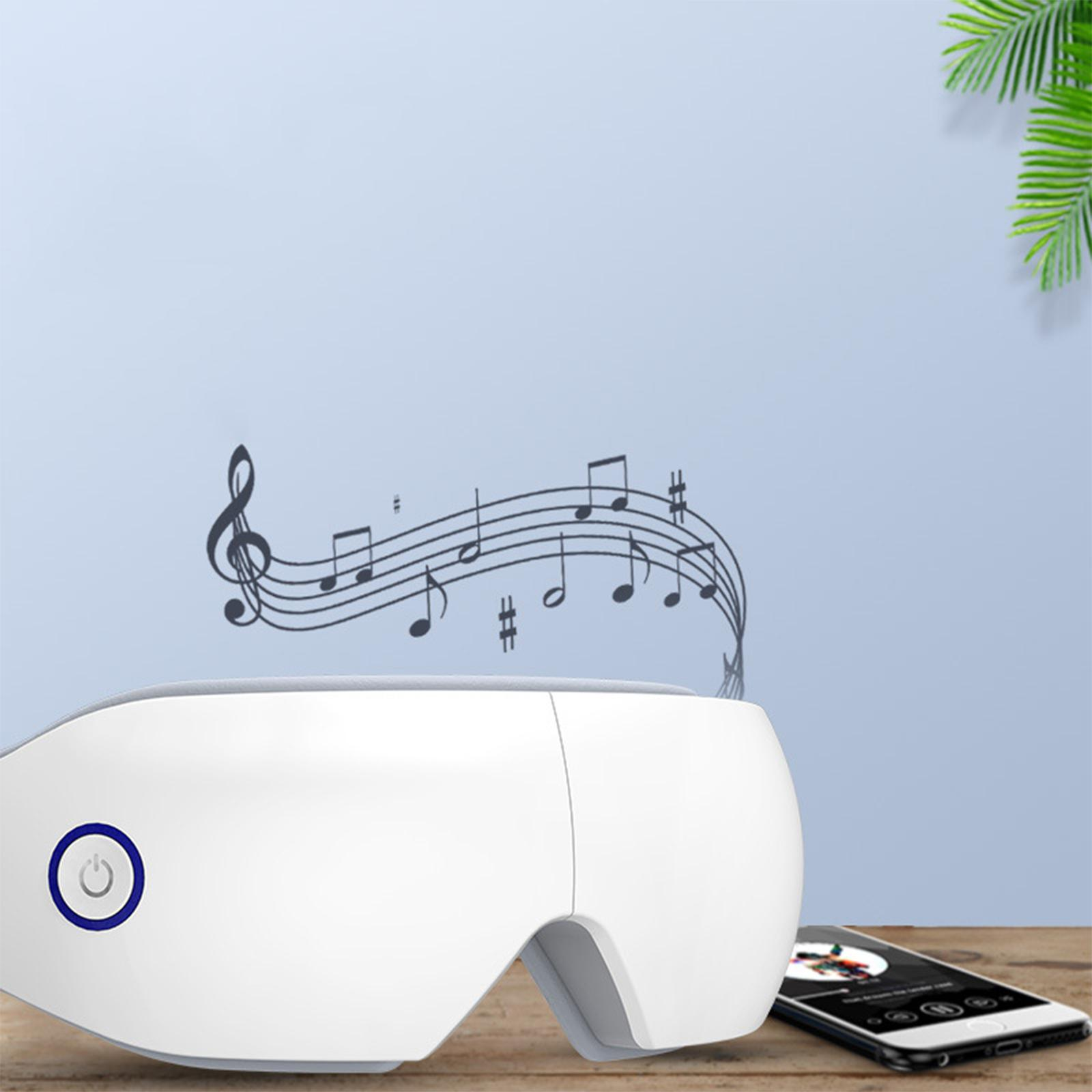 Weißes Augenmassagegerät mit Noten und Smartphone auf einem Holztisch. Im Hintergrund eine blaue Wand.