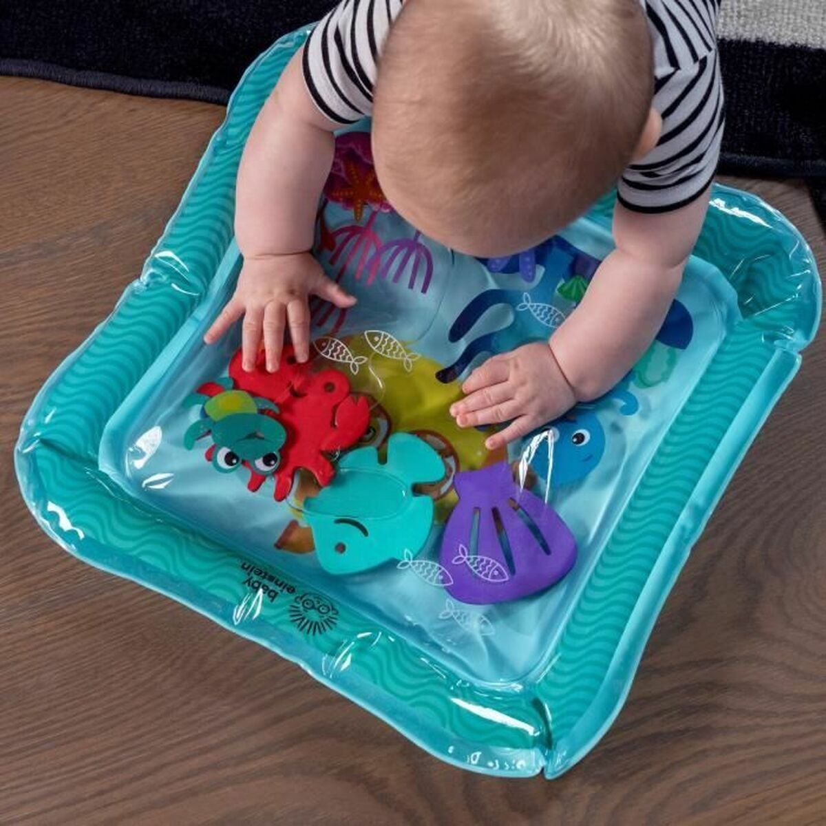 Baby in gestreiftem Hemd spielt in einer Wassermatte mit Meerestierspielzeug.