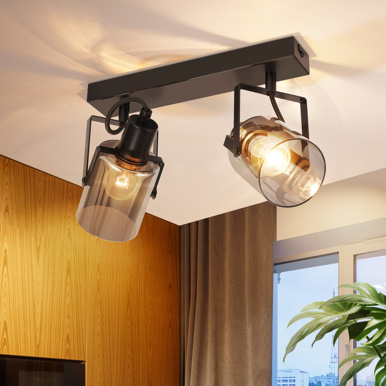 Due faretti da soffitto con paralumi in vetro e struttura nera, che illuminano una stanza con una parete in legno caldo.
