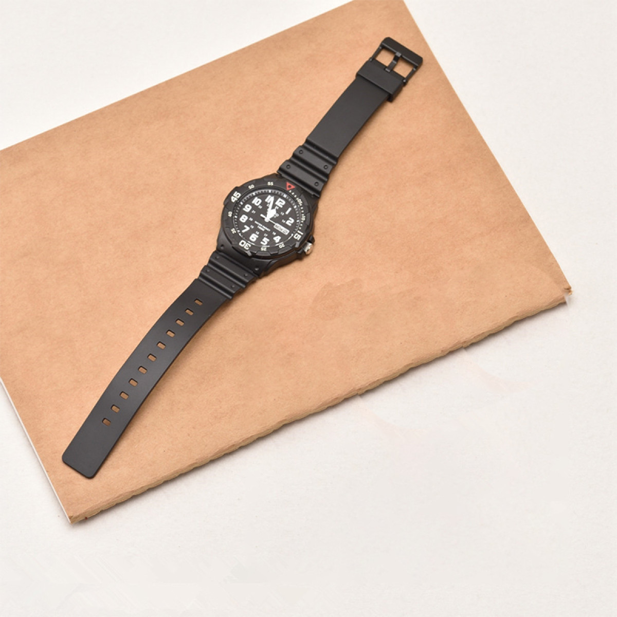 Schwarze Uhr auf braunem Papier. Die Uhr hat ein schwarzes Armband und ein schwarzes Zifferblatt.