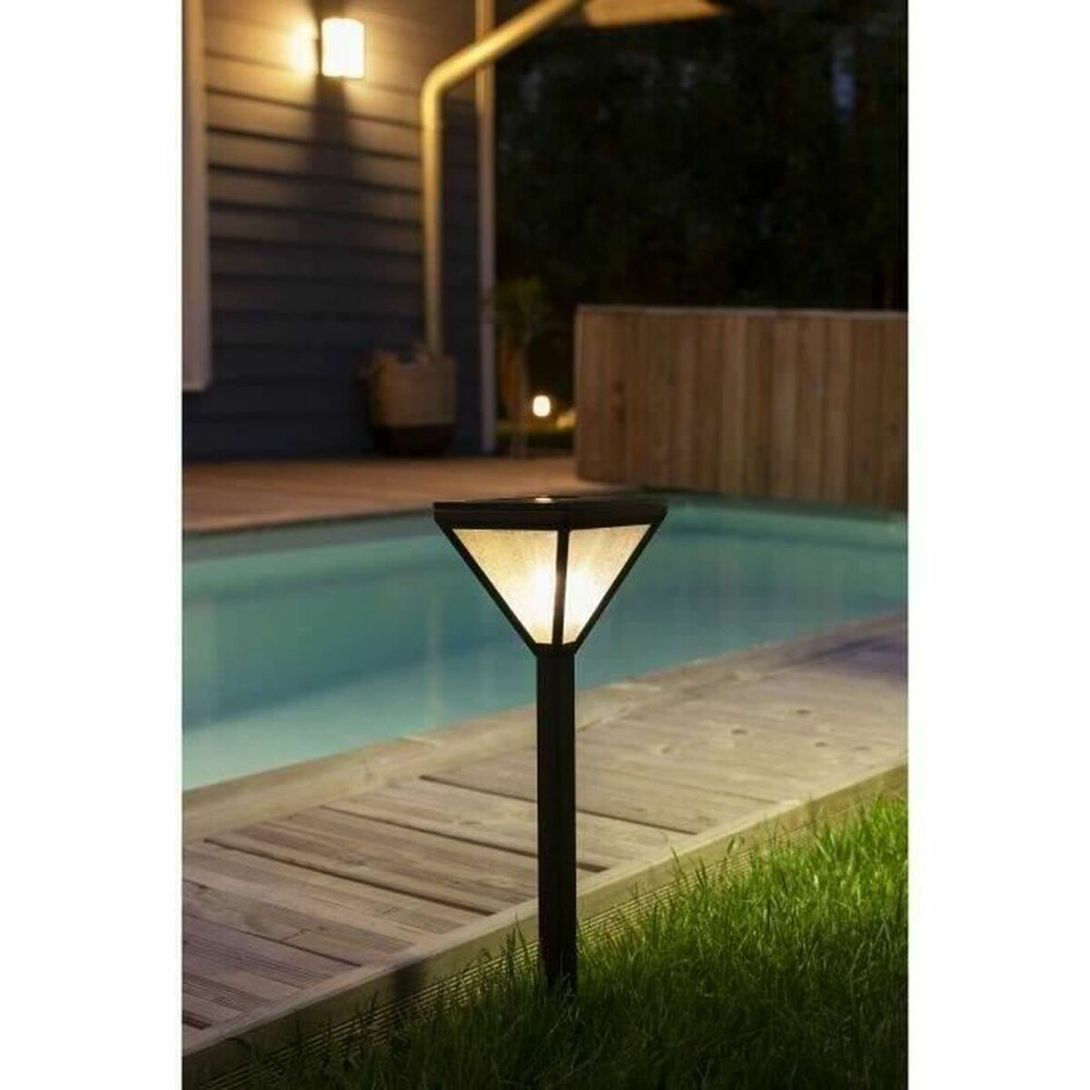 Eine Solar-Gartenleuchte beleuchtet einen Poolbereich. Sie hat eine dreieckige Spitze und einen Spieß.
