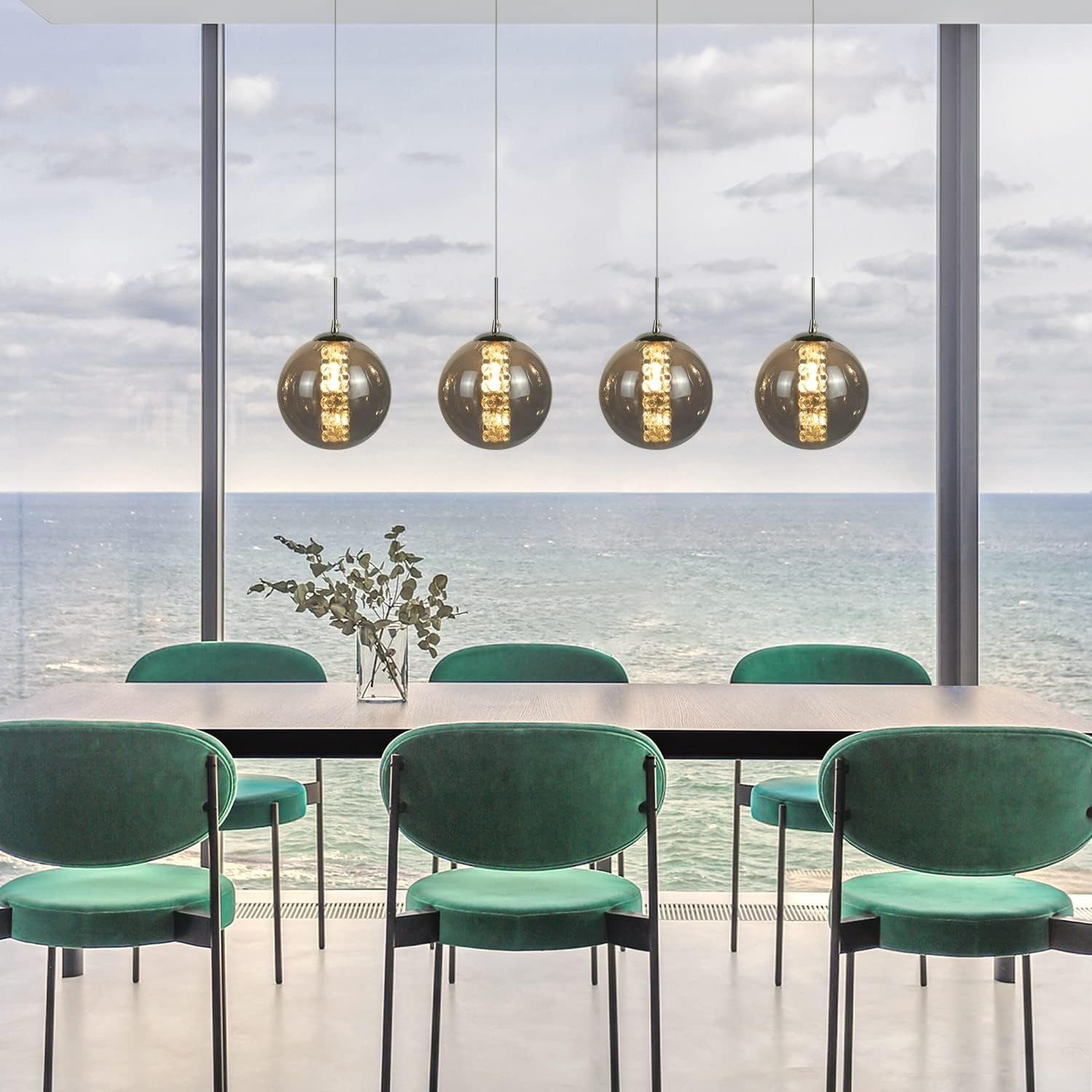 Sala da pranzo con tavolo, sedie verdi, lampade a sospensione e vista sull'oceano da una finestra.