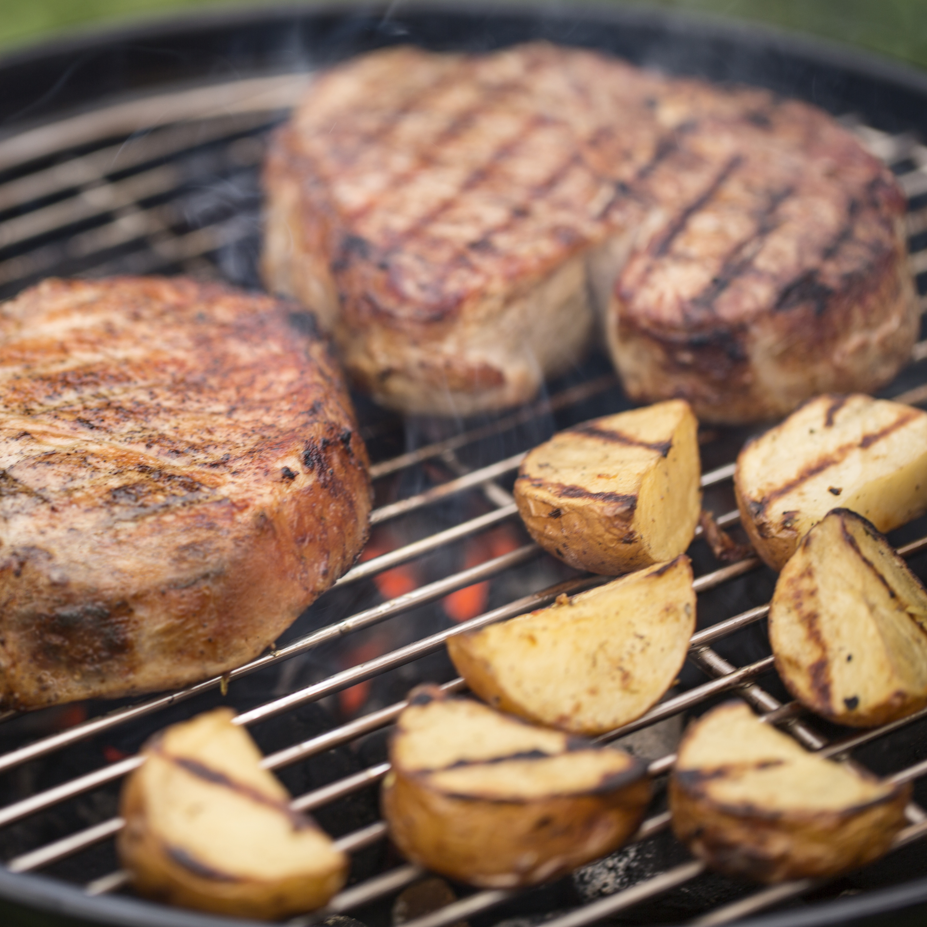Grillowane steki i ćwiartki ziemniaków na grillu, widoczne z bliskiej perspektywy.