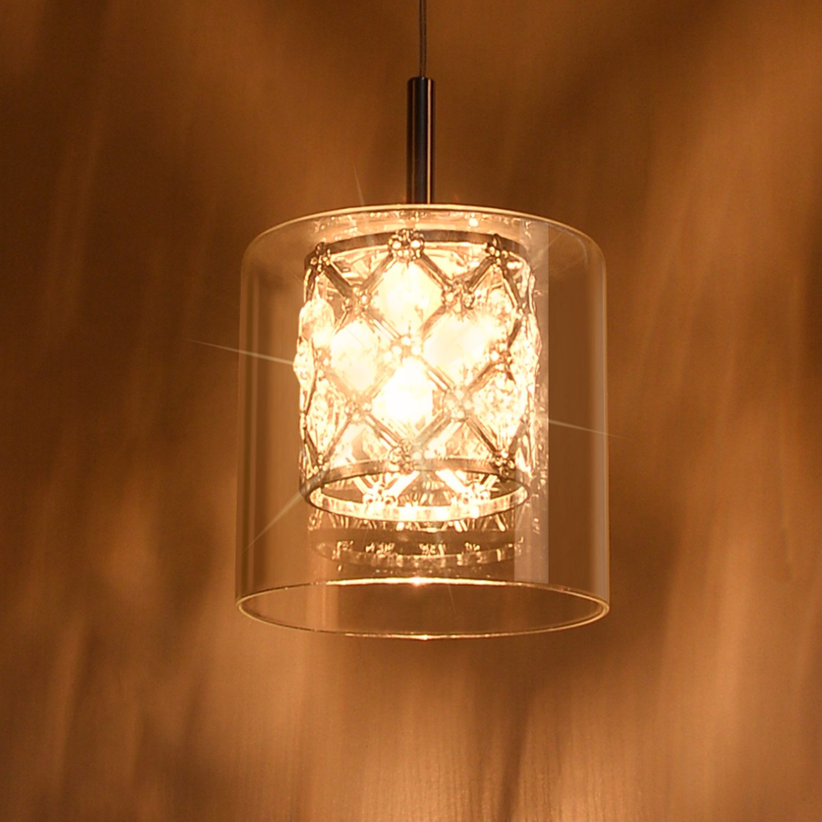 Una lampada a sospensione con paralume in vetro e un interno decorativo. La luce è accesa, illuminando la stanza.