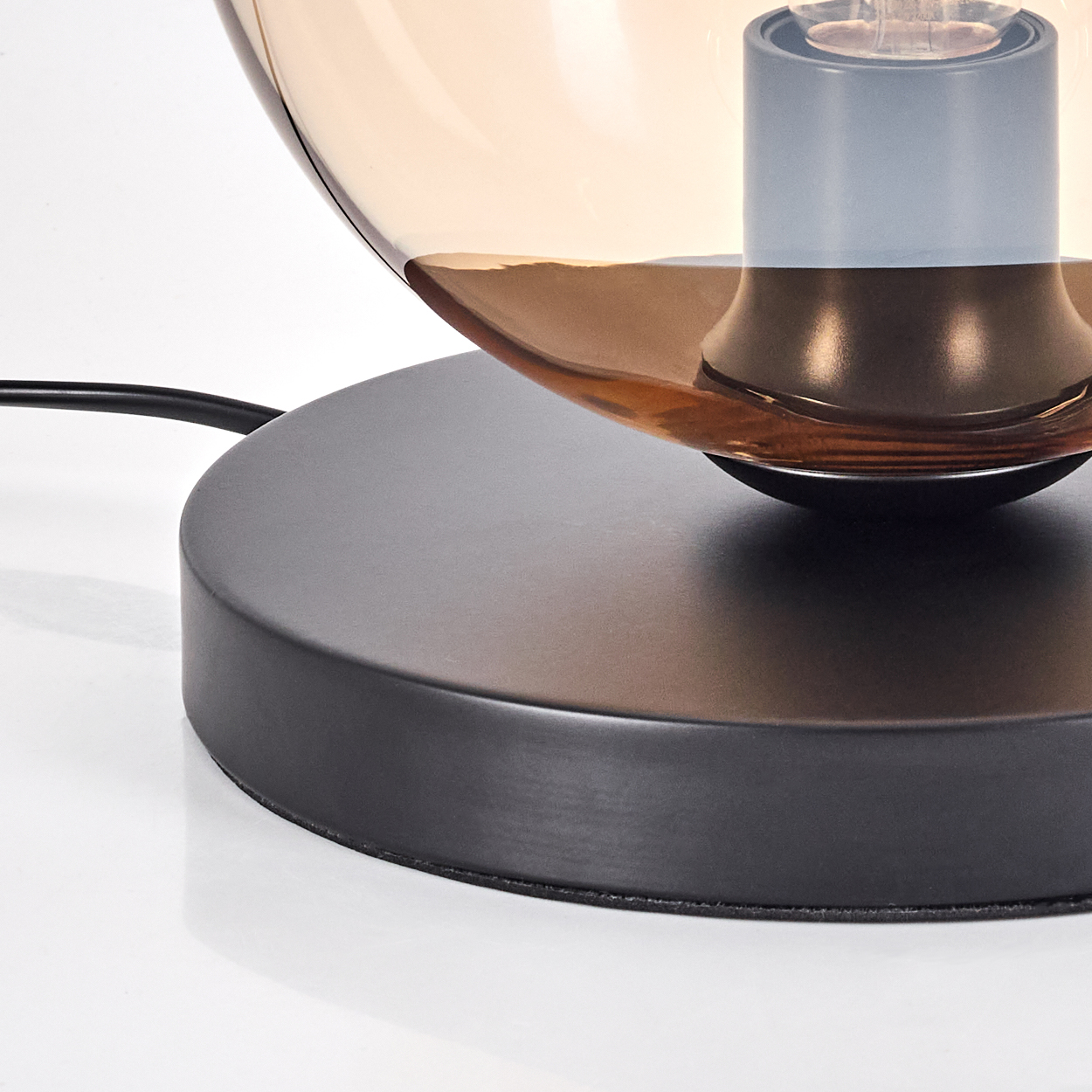 Eine Lampe mit dunklem Sockel und rundem Glasschirm, auf weißer Oberfläche.
