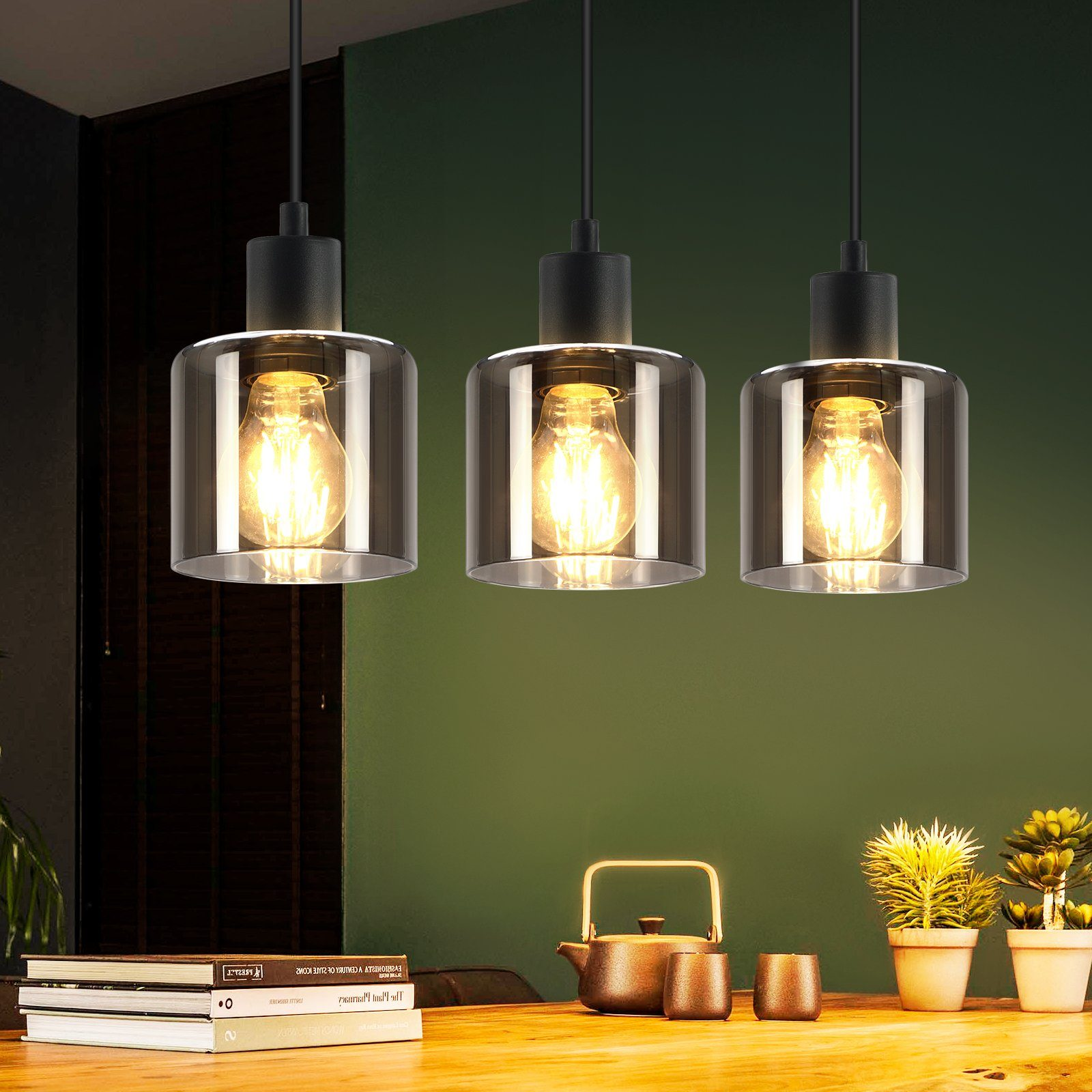 Tre lampade a sospensione con paralumi in vetro e lampadine visibili appese sopra un tavolo.