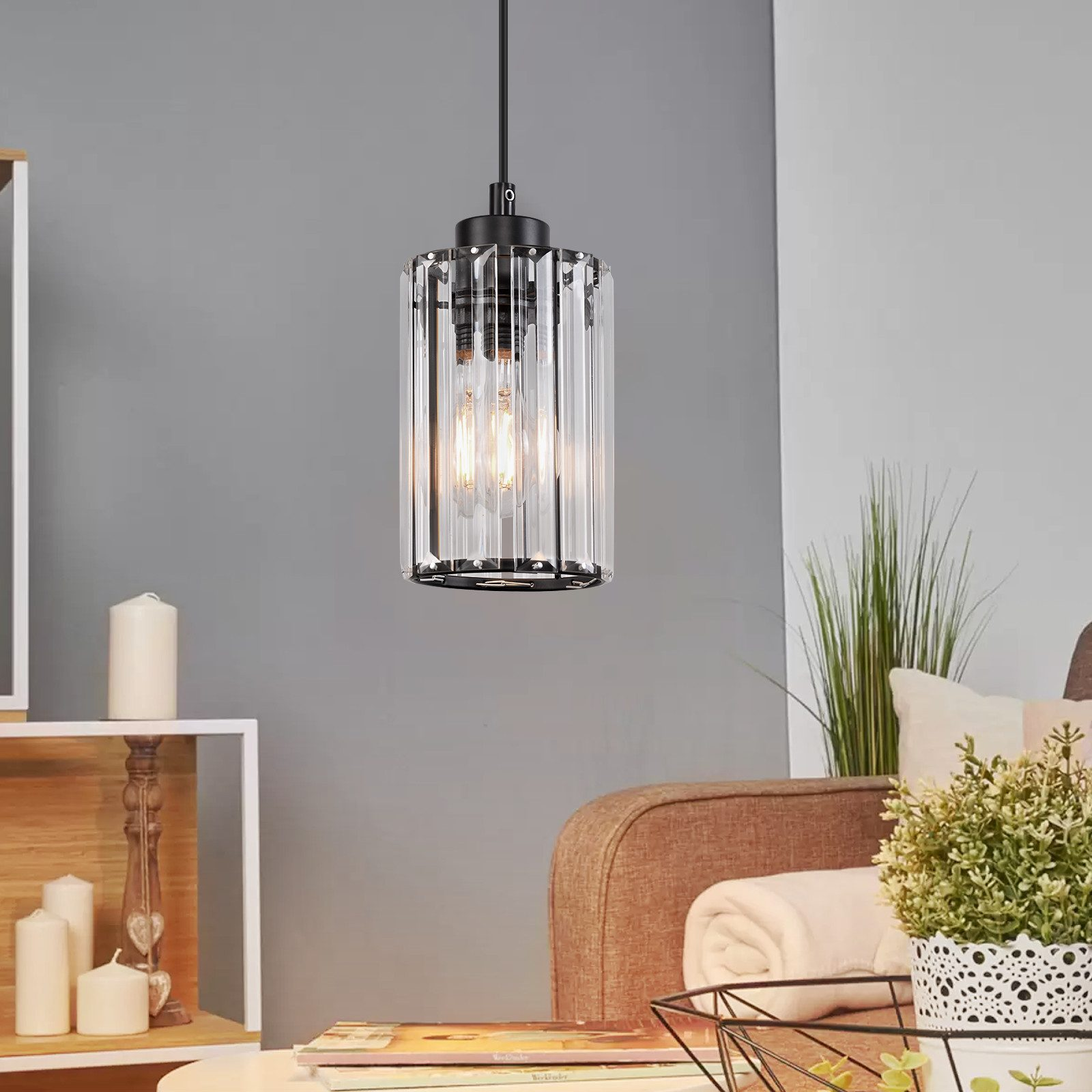 Una lampada a sospensione cilindrica è appesa in una stanza con un muro grigio. La luce ha vetro trasparente e lampadine.