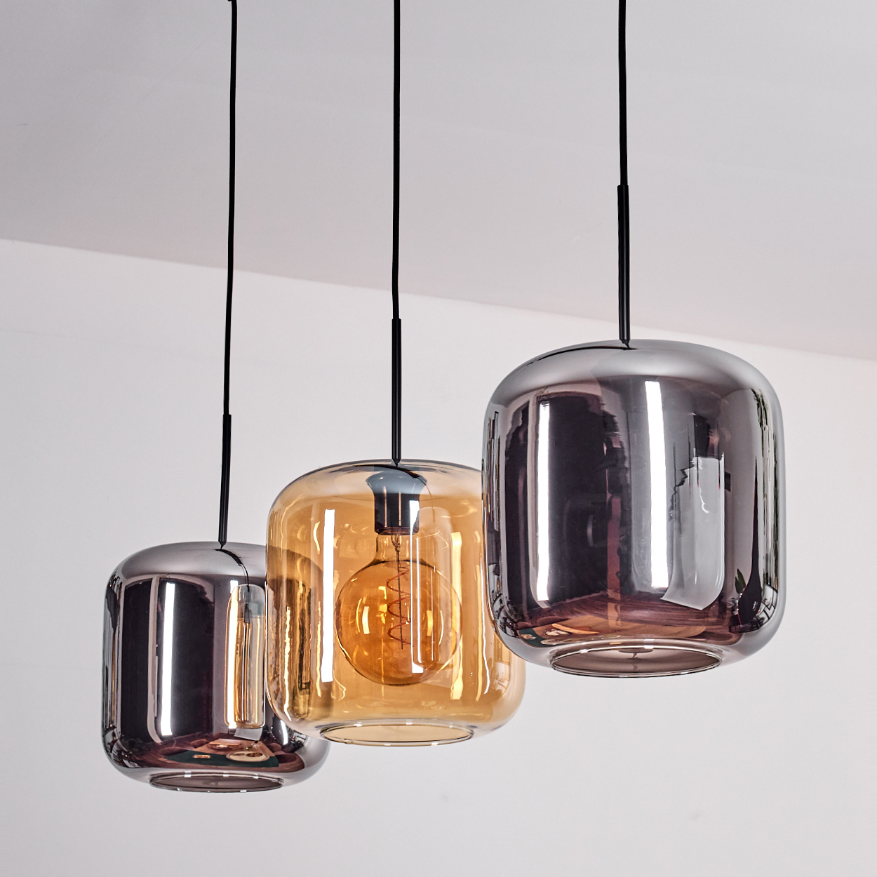 Drei Pendelleuchten mit Glasschirmen. Ein bernsteinfarbener, zwei Chrom, und hängende Drähte vor weißer Decke.