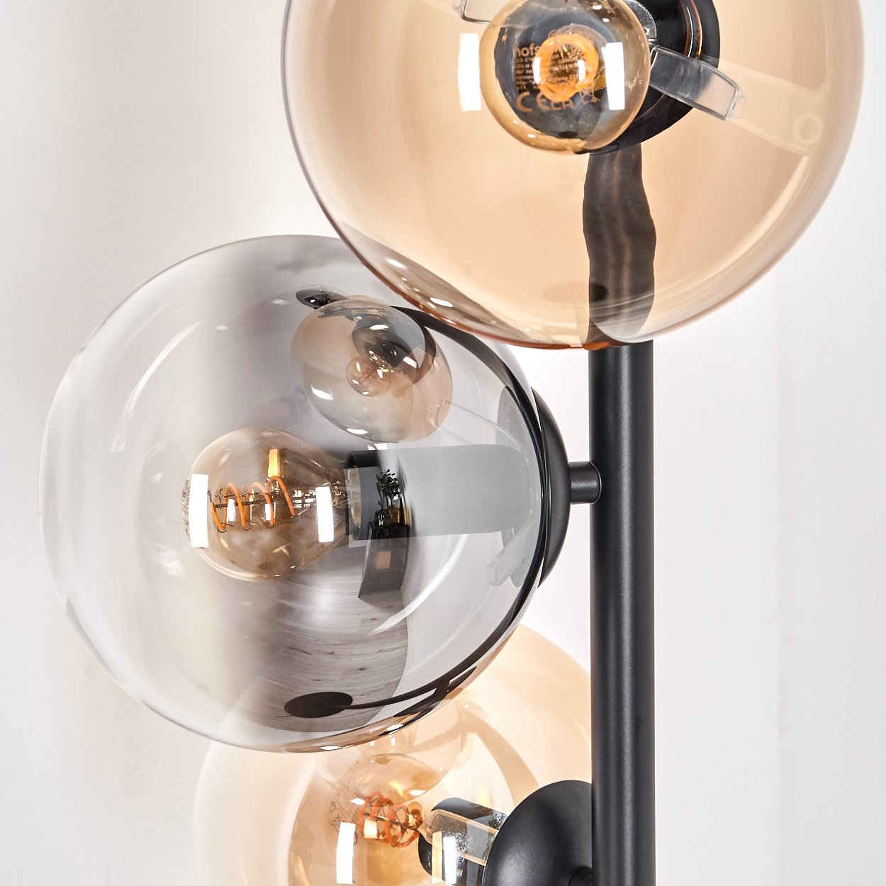 Nahaufnahme einer schwarzen Stehlampe mit bernsteinfarbenen und grauen Glaskugeln vor weißem Hintergrund.