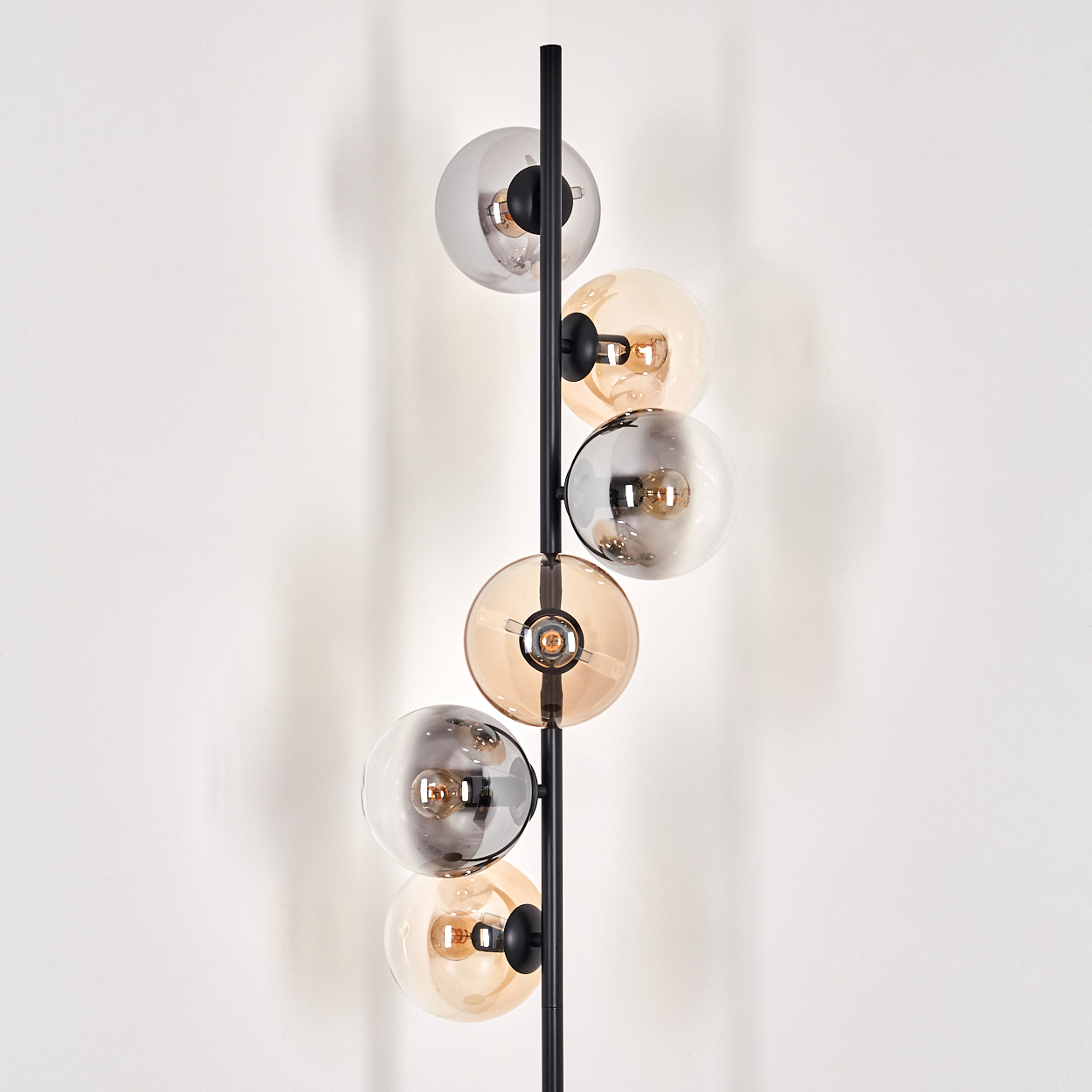 Eine schwarze Lampe mit bernsteinfarbenen und grauen Kugeln vor einer weißen Wand.
