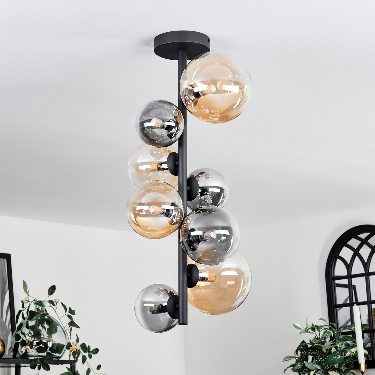 Schwarze Deckenlampe mit mehreren Glaskugeln in Bernstein und Silber. Helle, weiße Umgebung.
