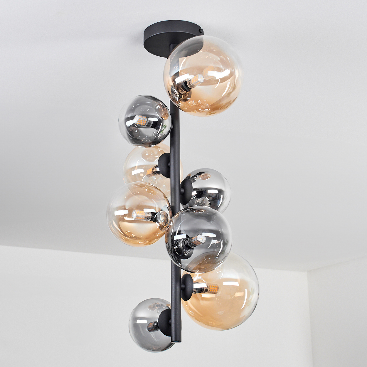 Deckenlampe mit bernsteinfarbenen und grauen Kugeln, die von einer weißen Decke hängt.